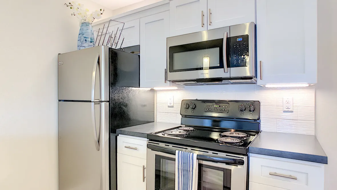 An up-close view of the stainless steel stove and built-in microwave, surrounded by white cabinetry and next to a stainless steel refrigerator.