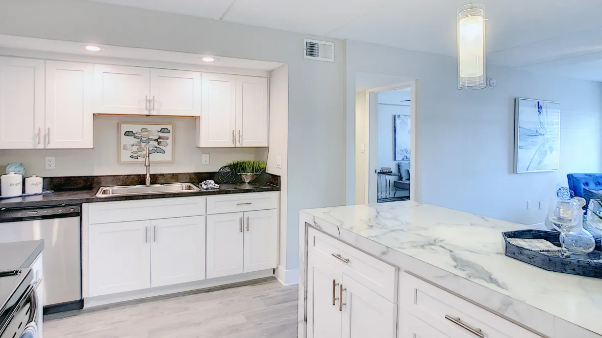 A view of the kitchen wall lined with ample white cabinetry from the breakfast bar, with the living room space in the background.