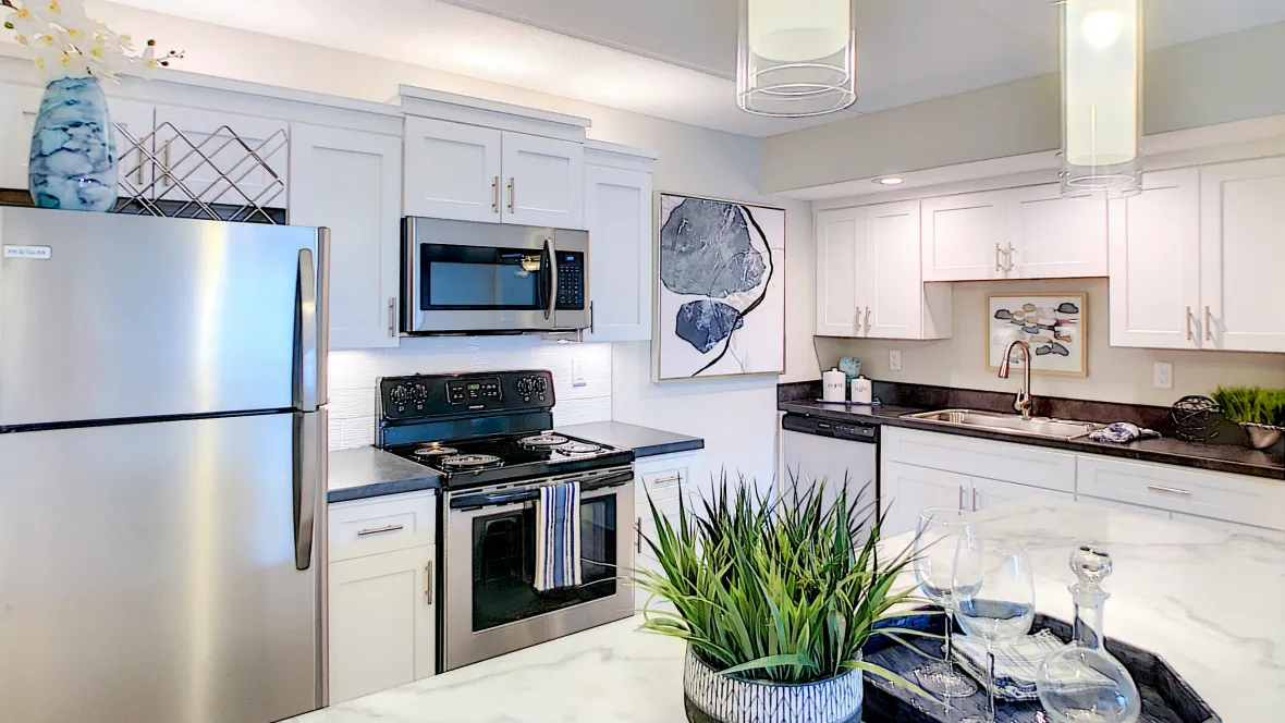A large kitchen with full stainless steel appliance package, white cabinetry, and modern light fixtures.