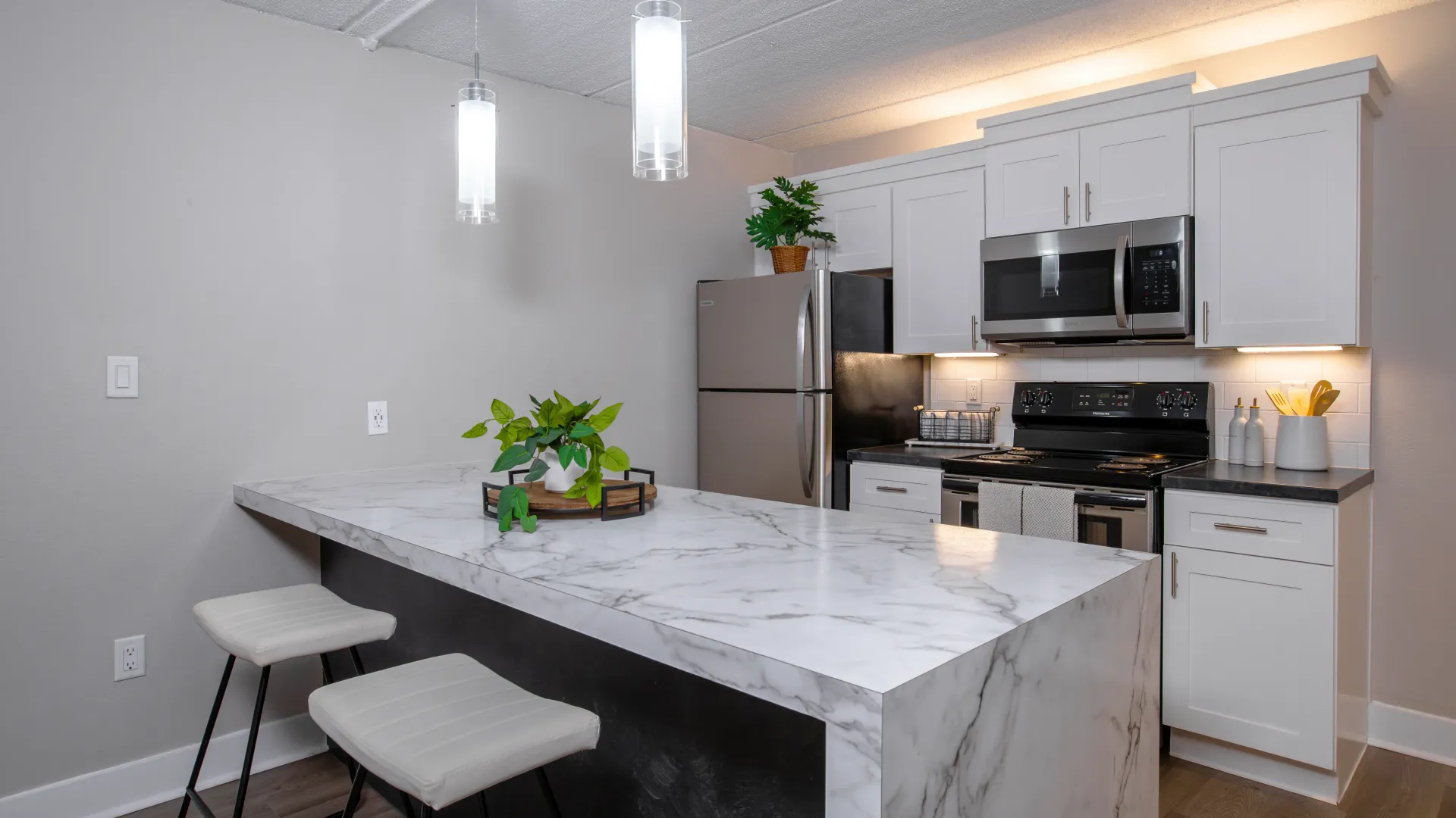 Modern kitchen with marble breakfast bar, stainless steel appliances, white cabinets, and pendant lighting at Elon Winter Park Apartments.