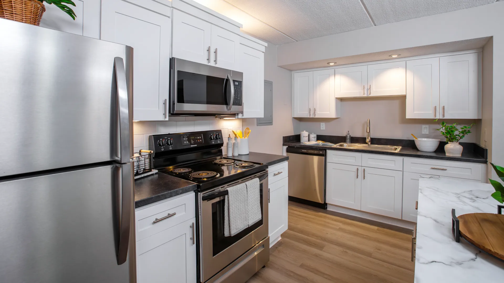 Modern kitchen with stainless steel fridge, microwave, and dishwasher, black granite countertops, and white cabinets at Elon Winter Park Apartments.