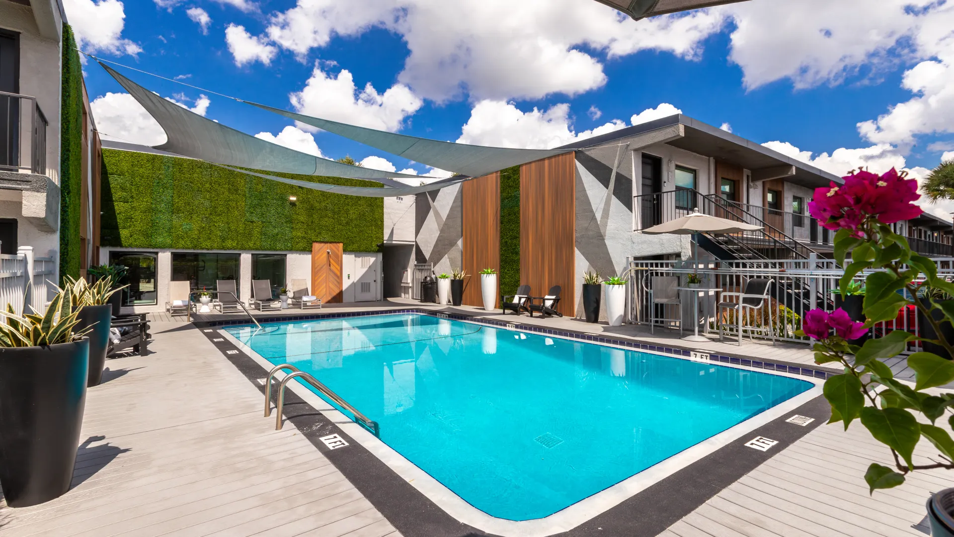 Expansive sundeck with resort-style pool, shaded lounge chairs, and vibrant landscaping at Elon Winter Park Apartments.