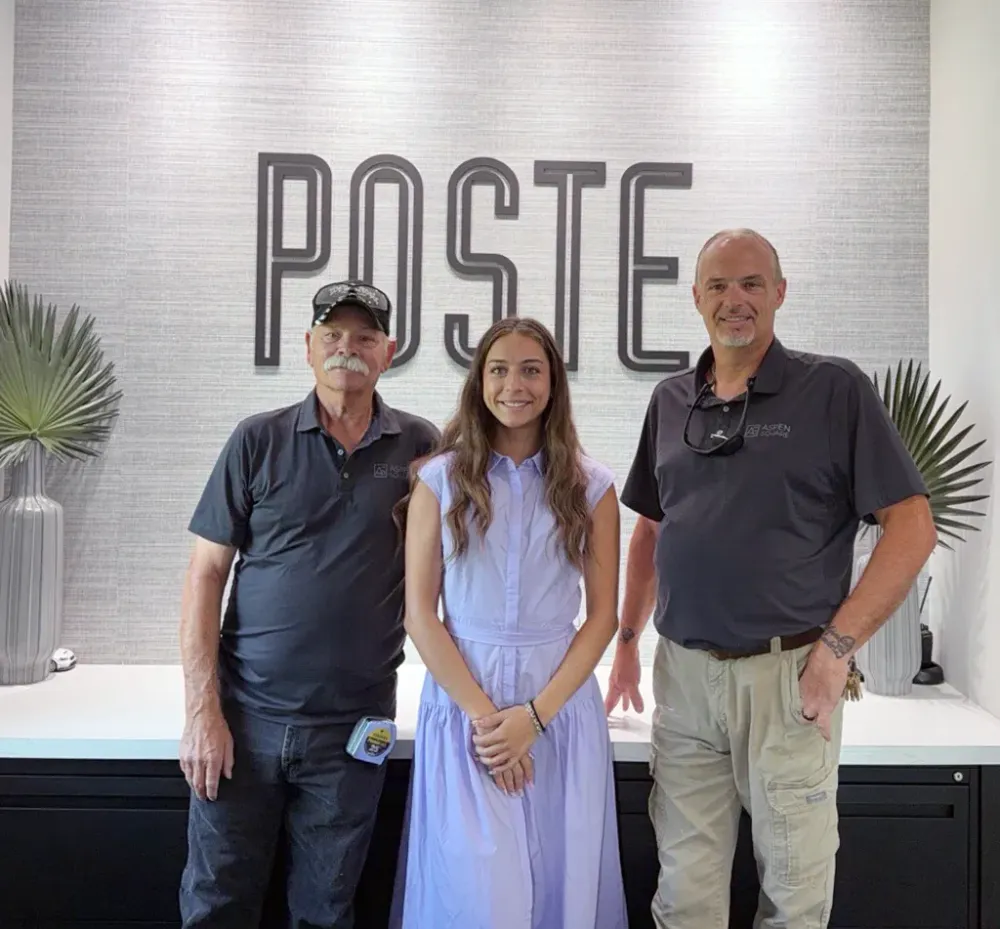 Poste Winter Park team members posing in the leasing office beside the community's branded wall display.