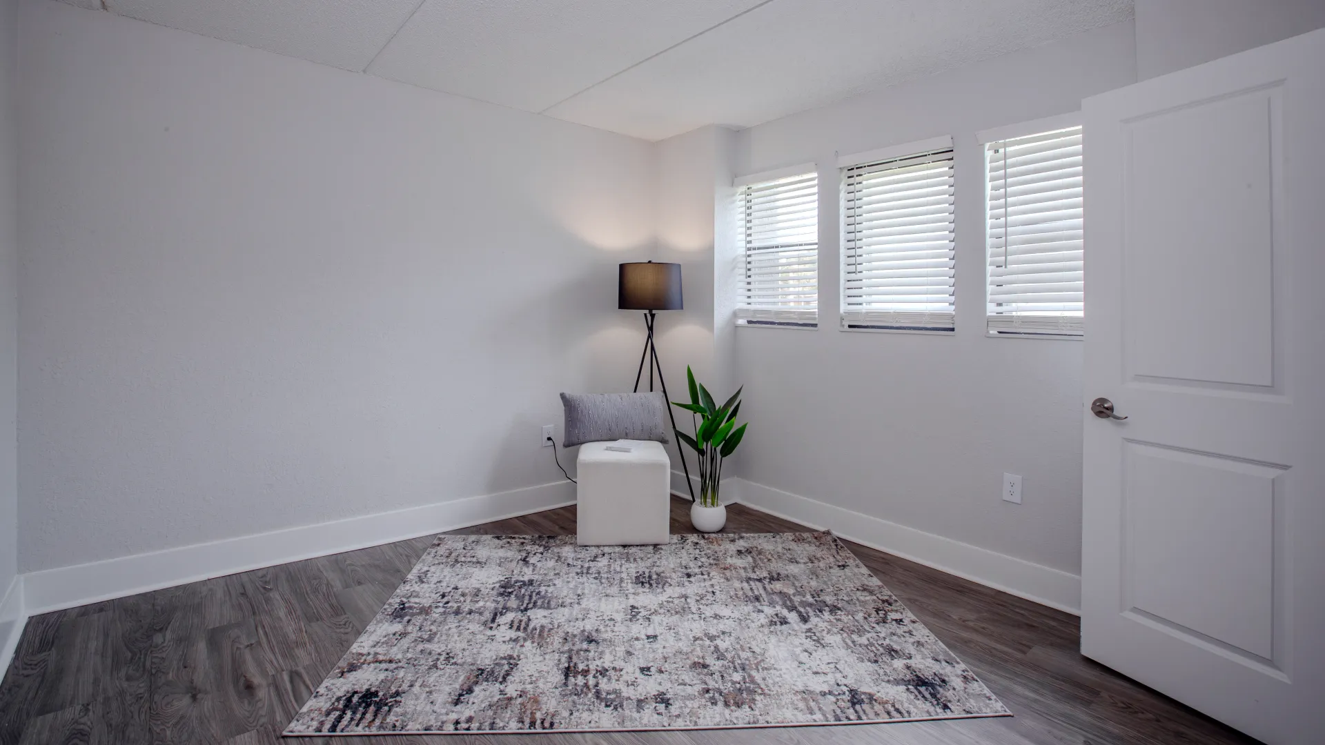 A cozy bedroom at Poste Winter Park featuring multiple windows, wood-style flooring, and a neutral decor with a soft area rug.