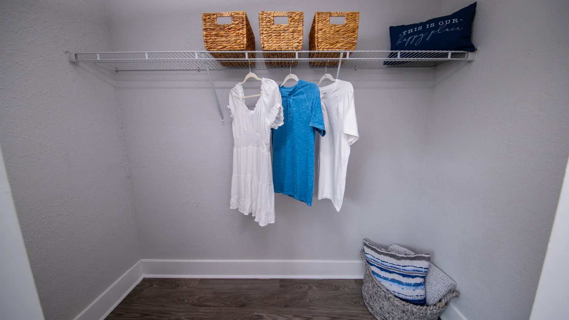 A spacious walk-in closet featuring ample hanging space with clothes and wicker storage baskets on the top shelf.