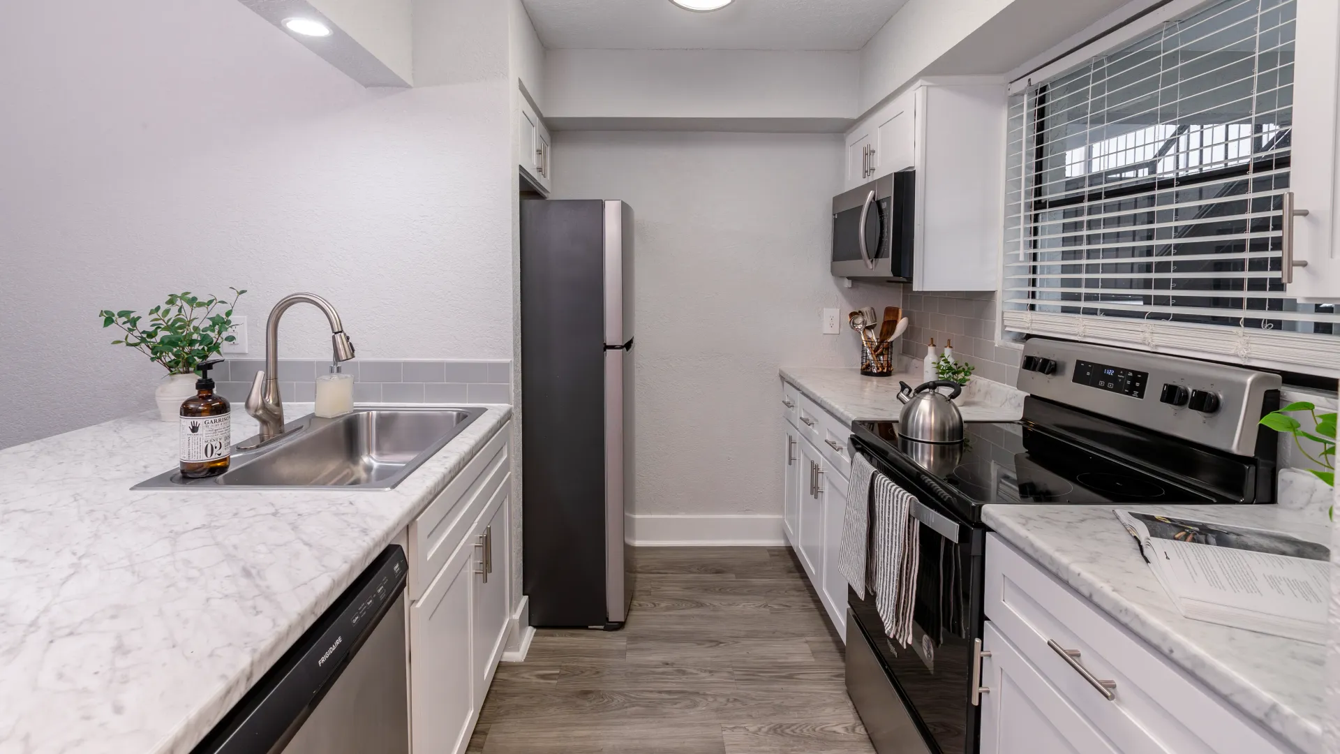 Modern kitchen with stainless steel appliances, marble-style countertops, and a tile backsplash, complete with a stainless-steel sink and stylish decor.