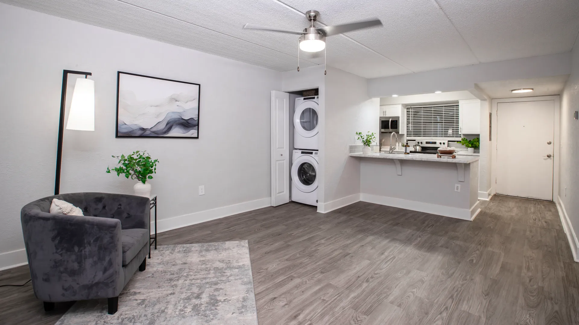 Open-concept living room at Poste Winter Park Luxury Apartments, featuring wood-style flooring, ceiling fan, and in-unit washer and dryer.