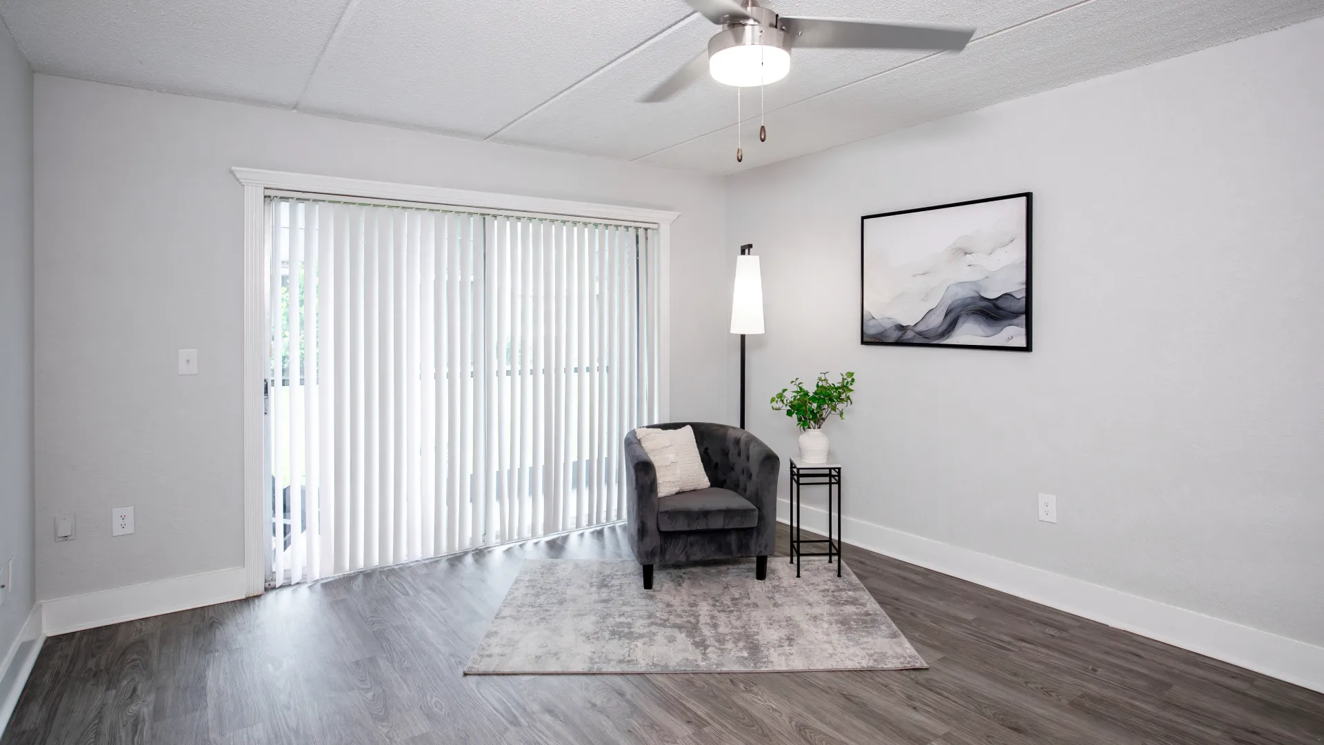 Living room with sliding glass doors leading to a private screened patio, featuring a gray armchair and modern decor.