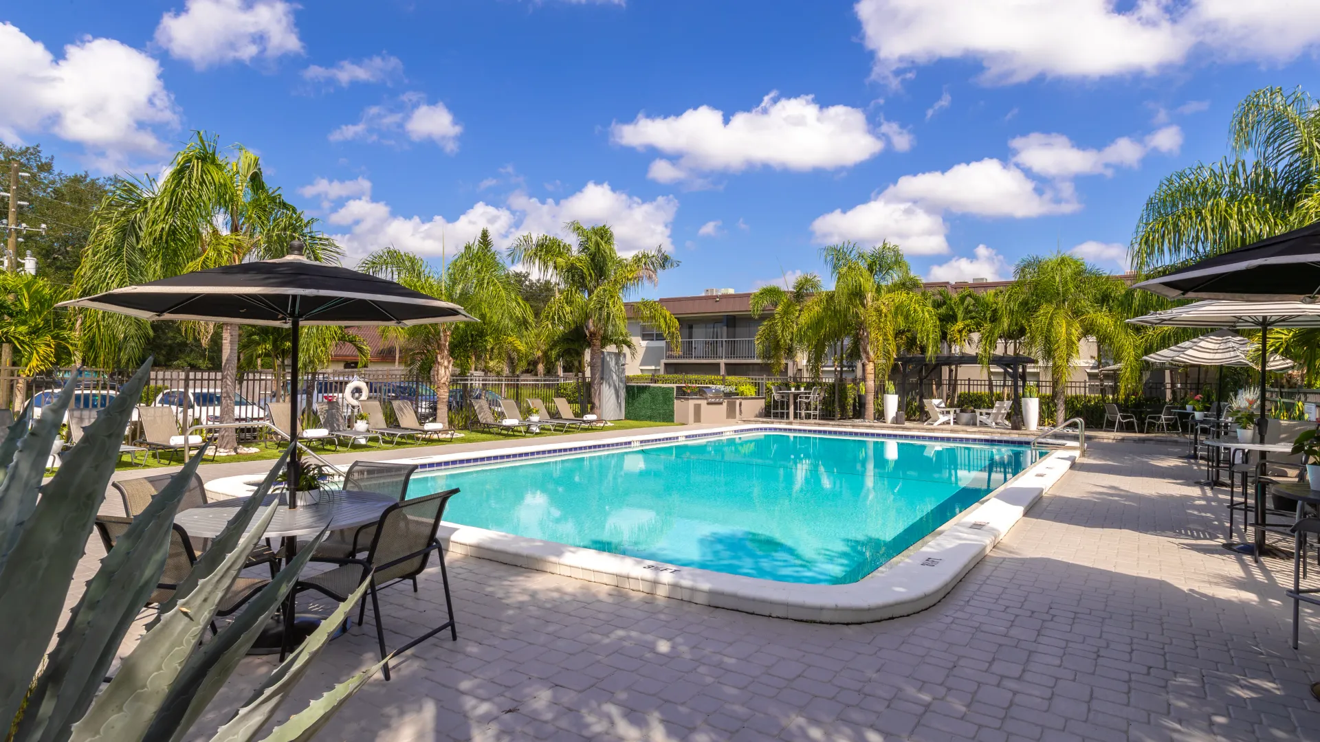 Resort-style pool with lounge chairs, shaded tables, and tropical landscaping, providing a relaxing and scenic outdoor space for residents.