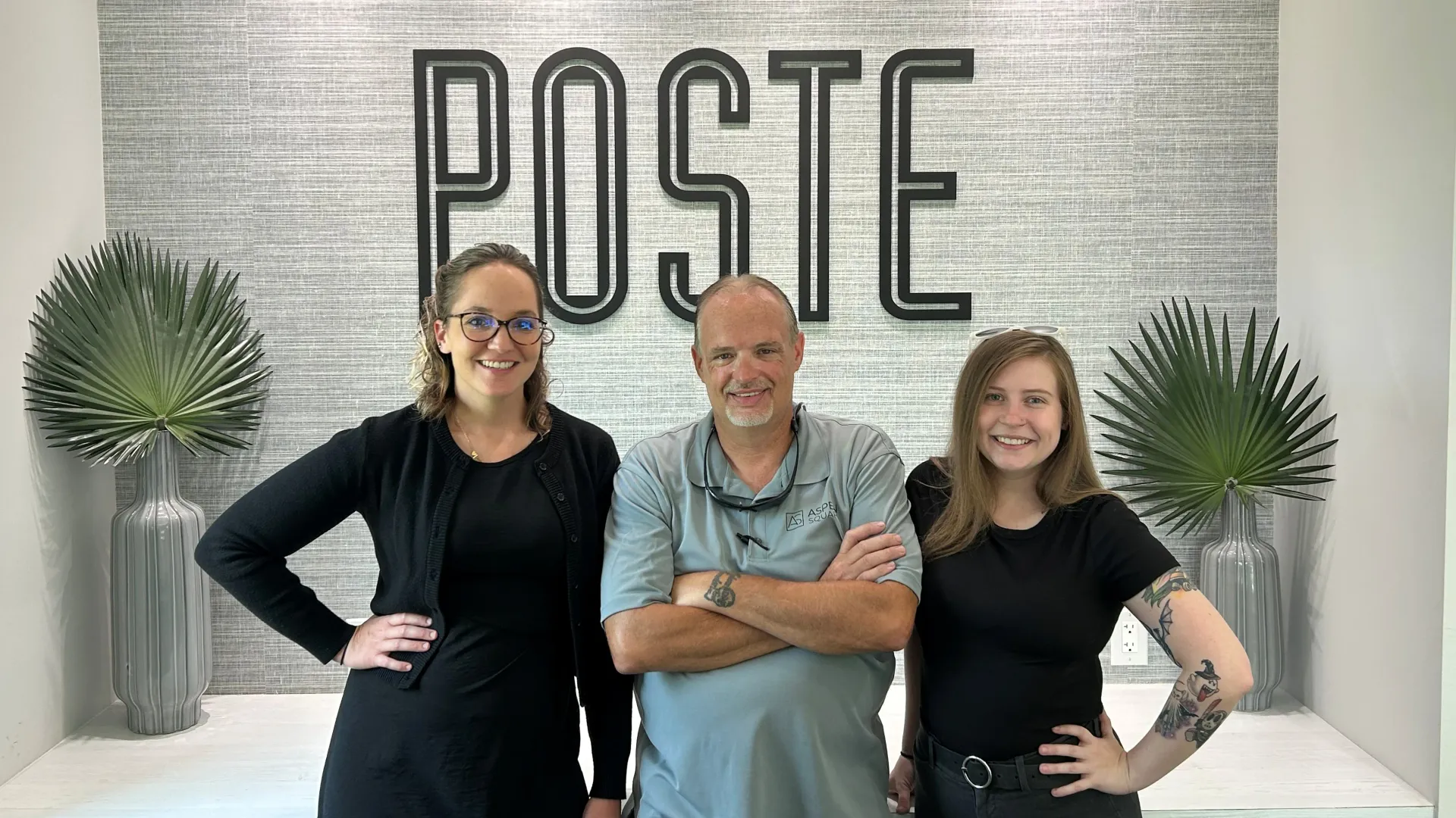 Three staff members of Poste Apartments smiling in front of the community sign inside the leasing office.