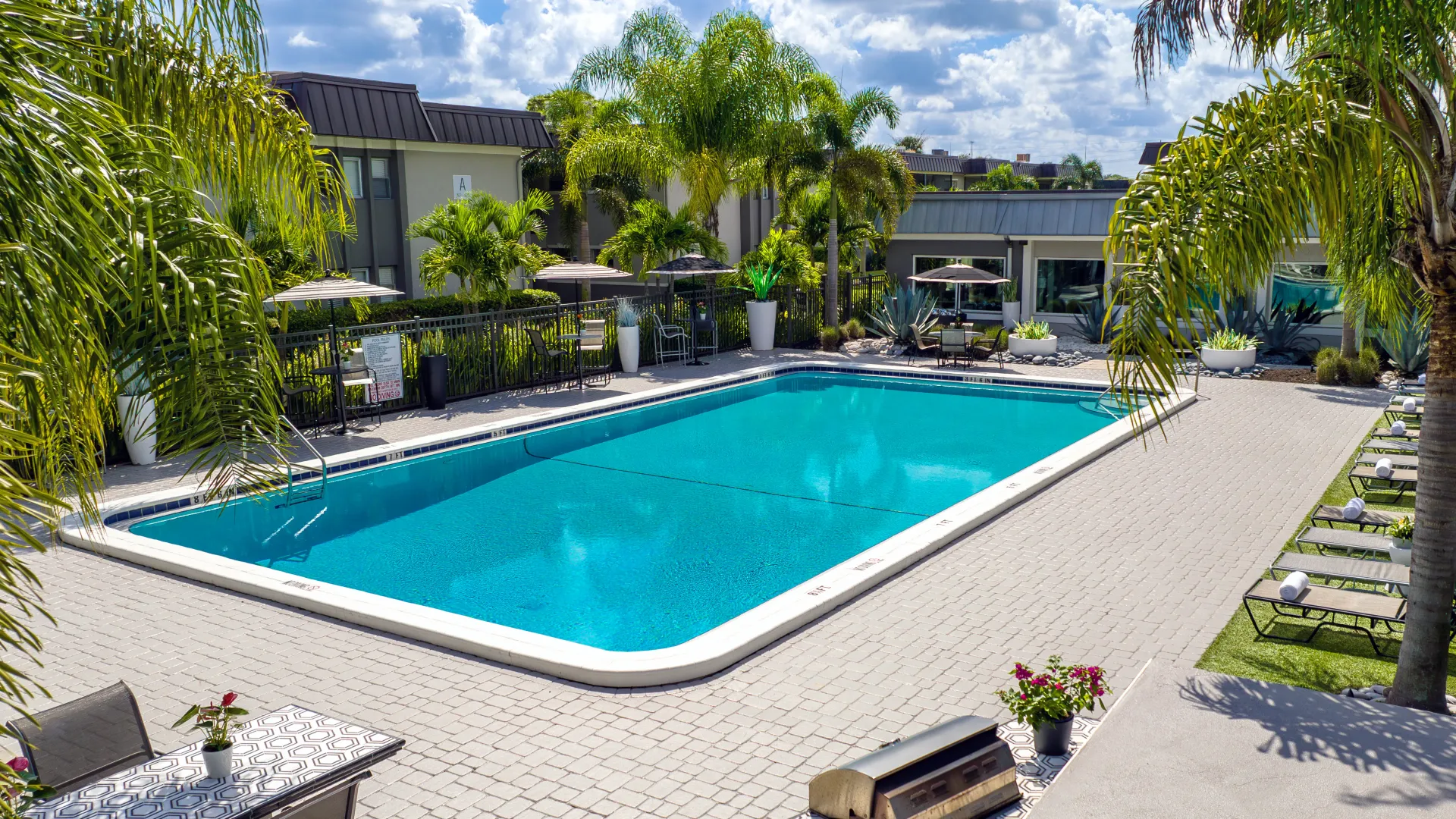 Resort-style pool and sundeck with tropical landscaping, lounge chairs, and shaded seating areas, offering a relaxing outdoor space for residents.