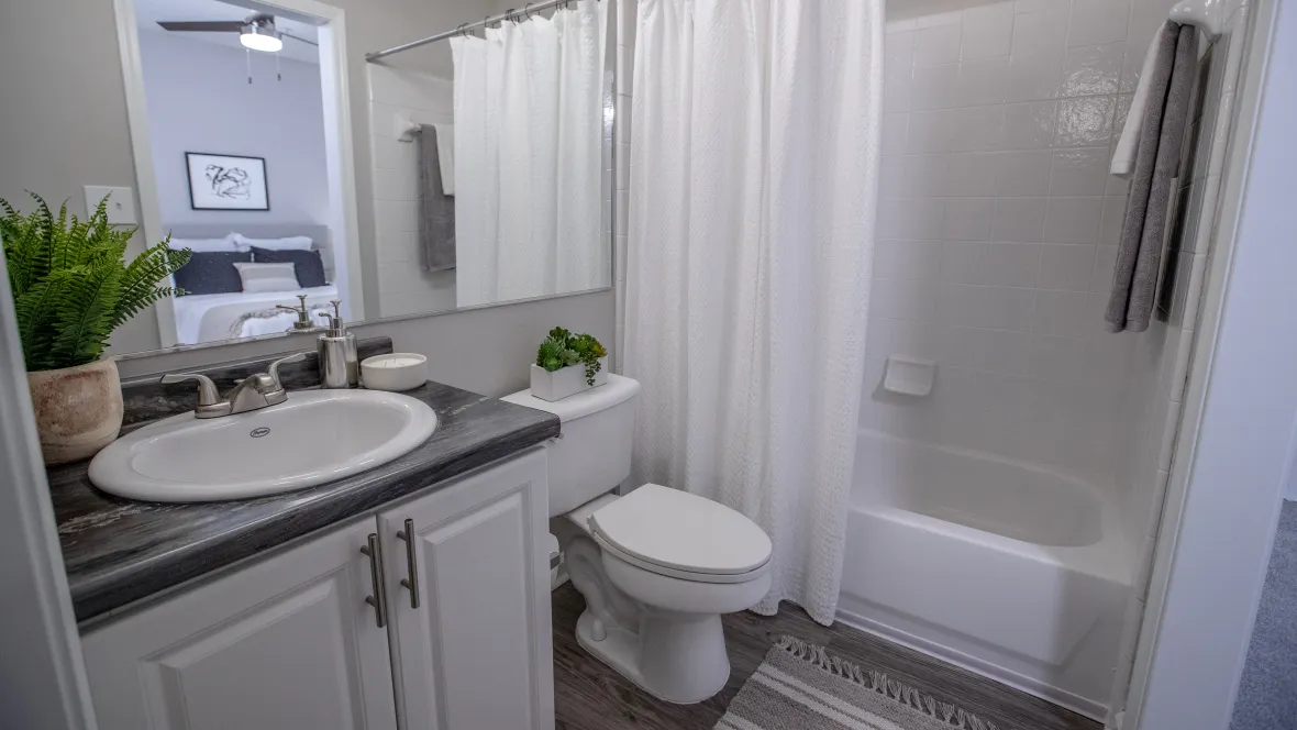 A sleek, modern bathroom adorned with spacious white cabinets beneath roomy black fusion granite-inspired vanity, a vast mirror, and a white tile surround shower/tub combo, creating a refined, updated appeal.