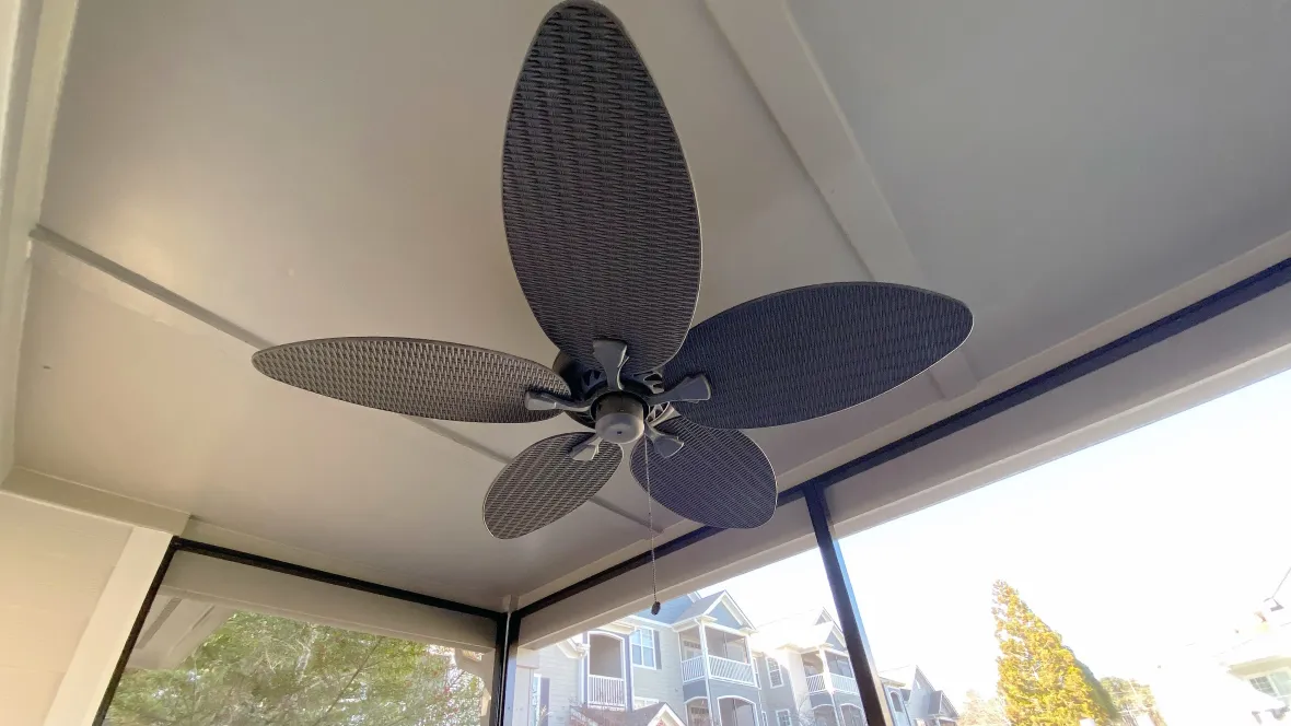 A large outdoor-rated ceiling fan with wide leaf-like blades on a screened-in patio ceiling.