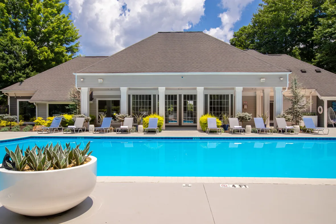 A sparkling blue pool with poolside loungers lining the pool deck across the water.