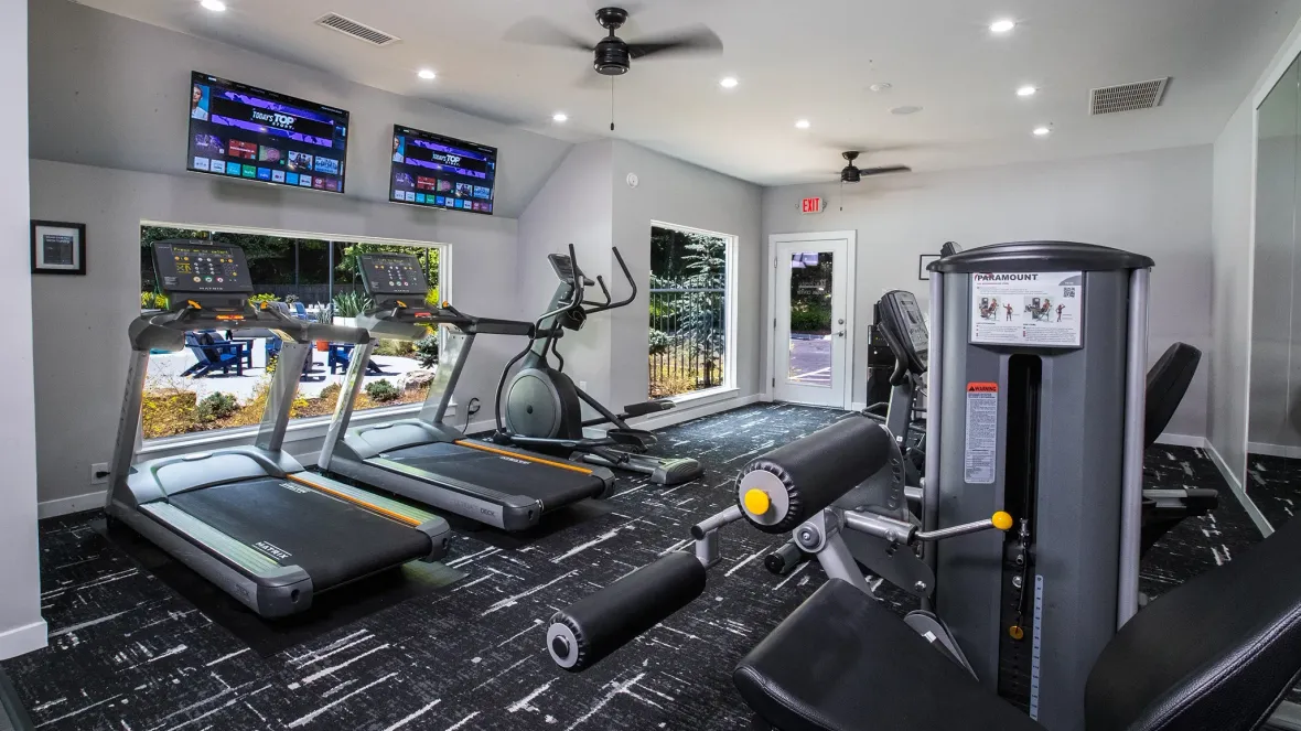 Fitness center with 2 treadmills, and elliptical, and all-in-one weight machine, facing 2 televisions mounted above large windows that overlook the pool deck