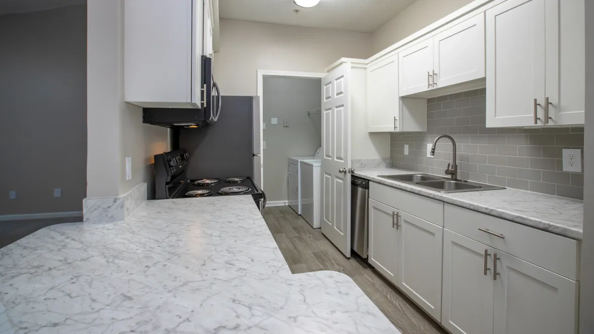 A view of a kitchen with Carrara marble inspired countertops, grey tiled backsplash, and stainless steel appliances from the large breakfast bar.