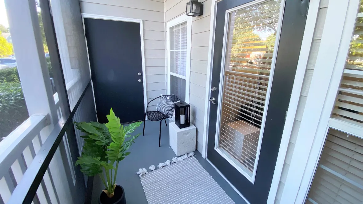 A screened-in patio space with glass door leading to an apartment's living room.