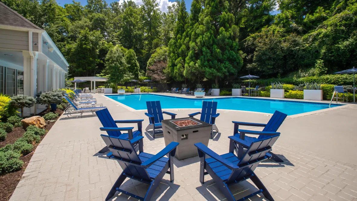 A firepit surrounded by six Adirondack chairs next to the pool.