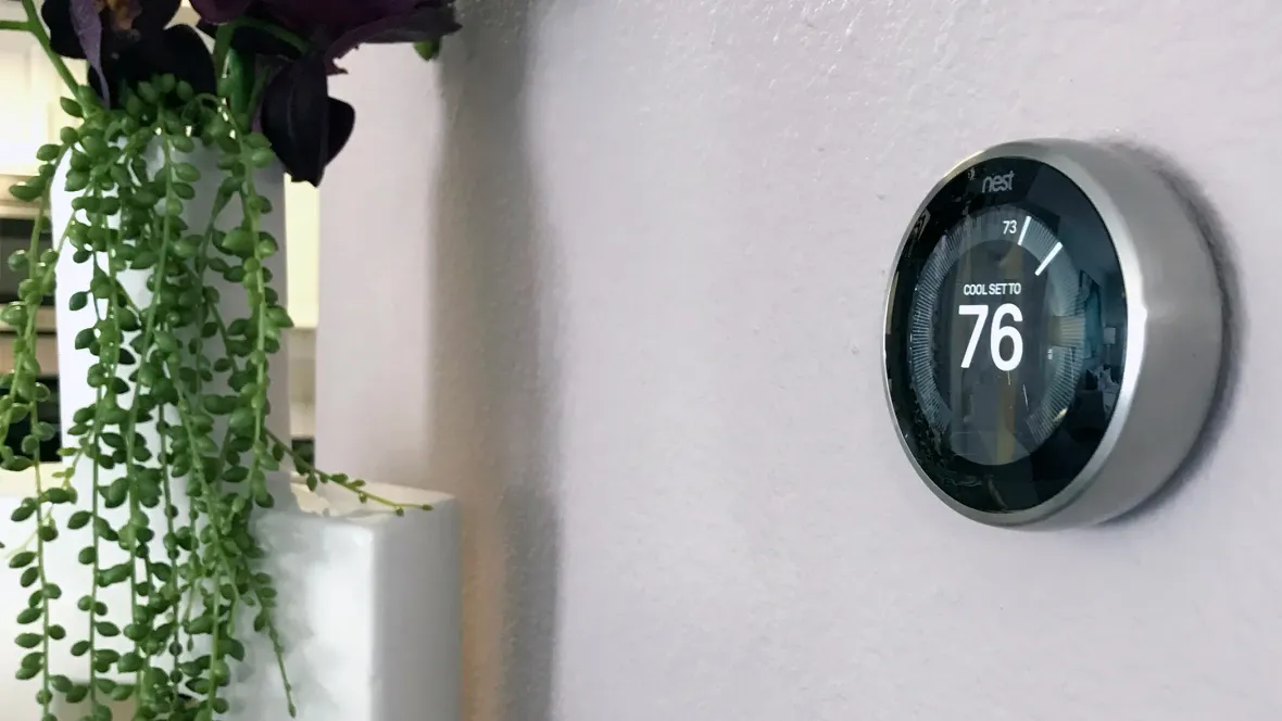 A Nest brand smart thermostat hanging on the living room wall of an apartment home