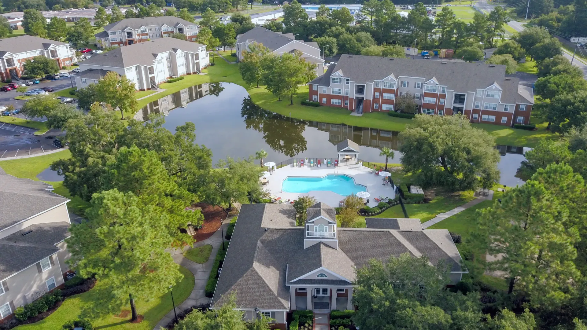 An aerial masterpiece of Eagle's Pointe's coastal bliss: lush landscapes, serene lake, playground for children, resort-style pool, and immaculate apartment buildings – amidst nature's beauty. 