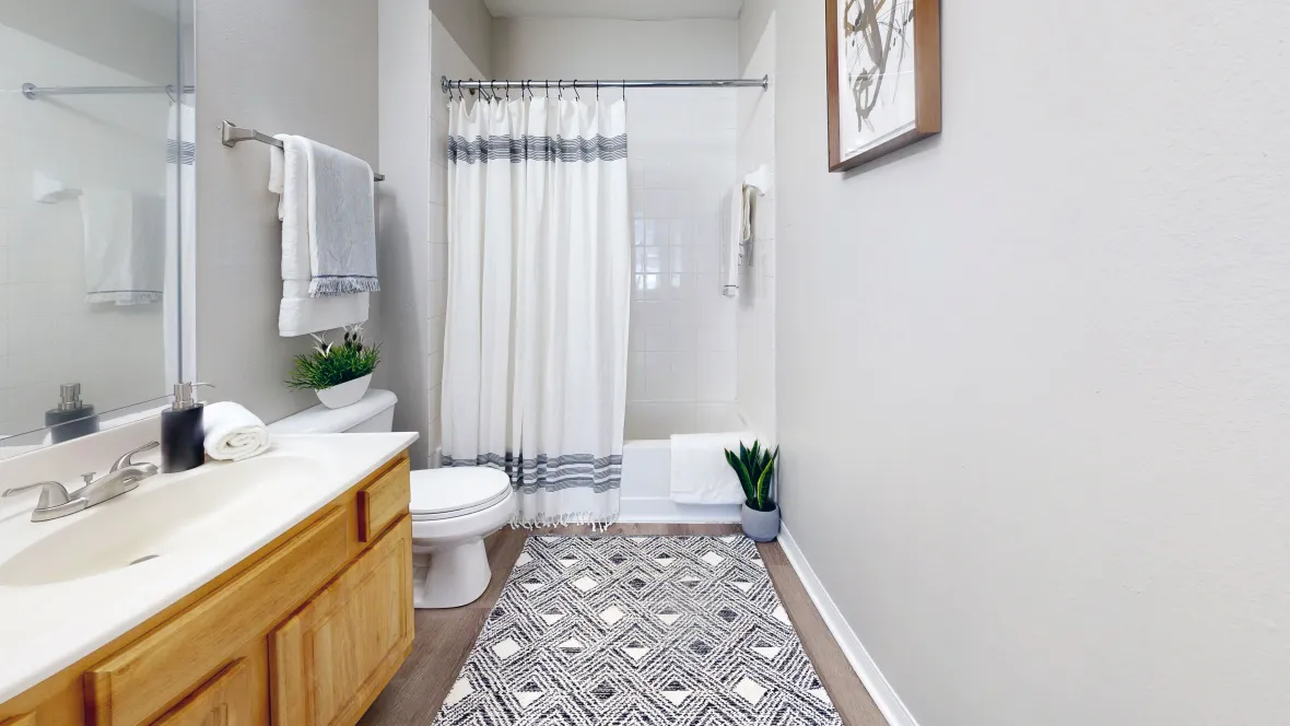 A spacious bathroom featuring a sleek shower/tub combo, large mirror, and a touch of serenity.