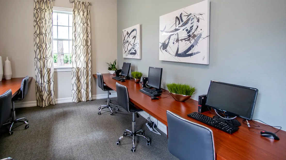 A spacious business center at Eagle's Pointe, featuring multiple computer stations, extensive desk space, workstations, and cozy office chairs for a productive work environment.