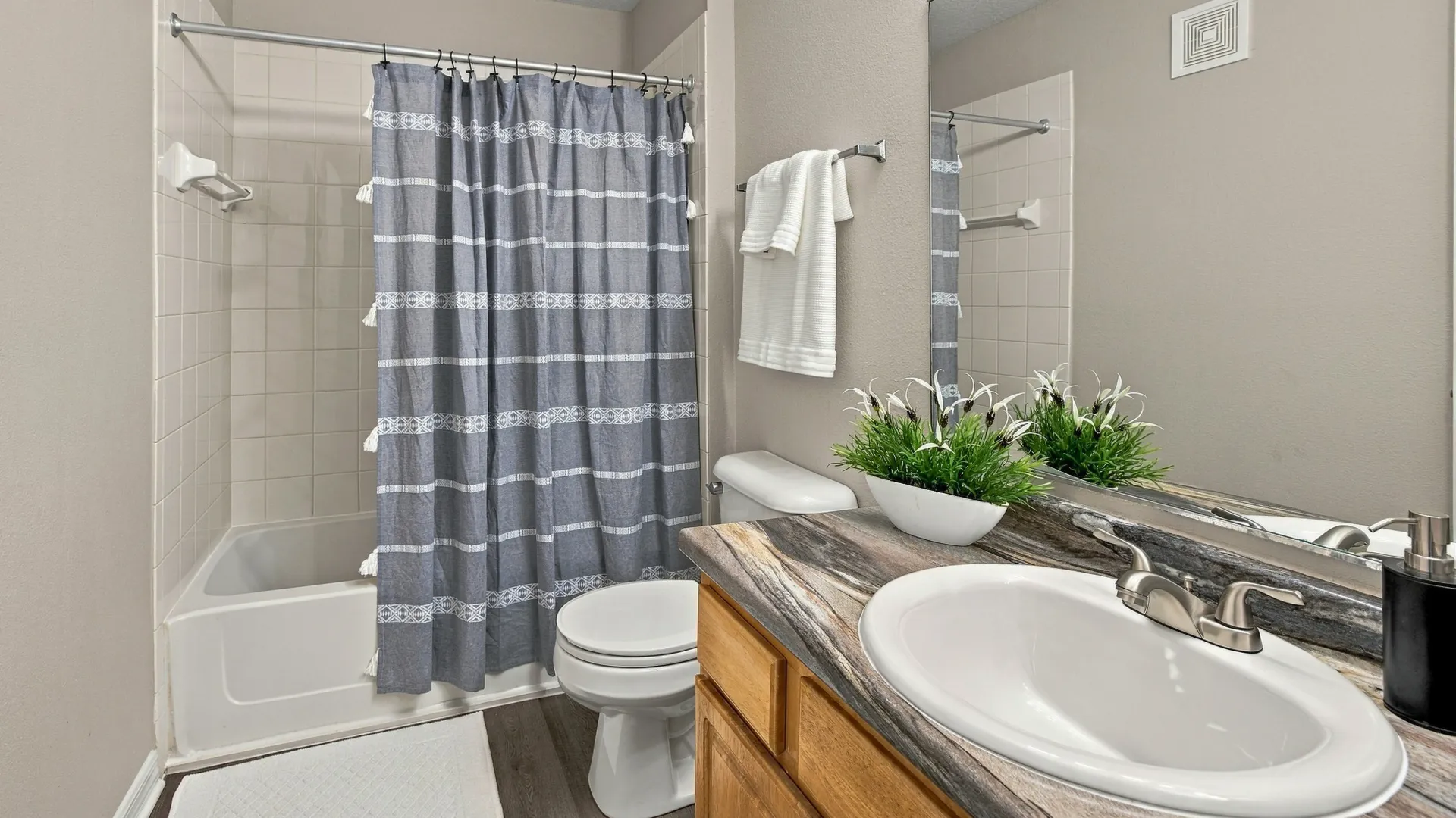 Apartment bathroom at Eagle's Pointe with a large vanity, decorative countertop, wood cabinetry, oversized mirror, and tiled tub-shower combination.
