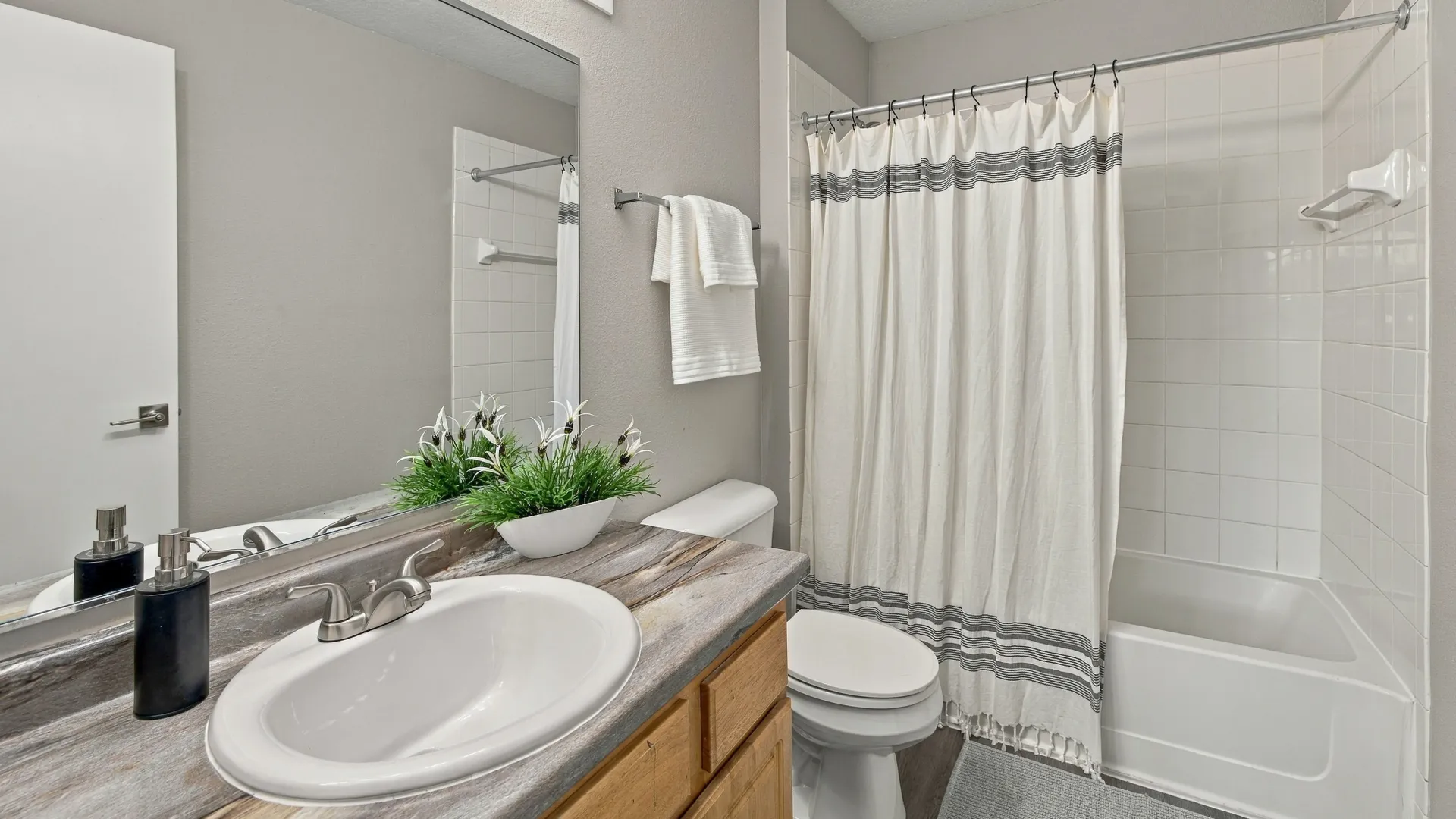 Primary bathroom at Eagle's Pointe featuring a spacious vanity with ample counter space, wood cabinetry, a large mirror, and a tiled tub-shower combination.