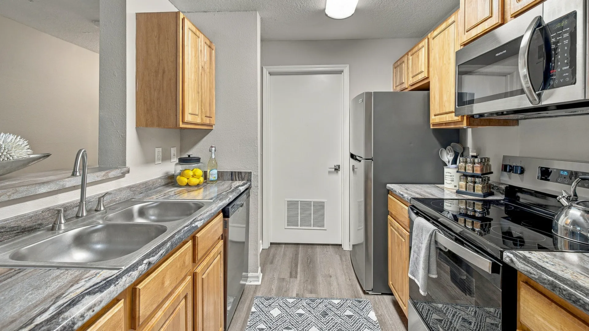 Kitchen at Eagle's Pointe featuring stainless steel appliances, wood cabinetry, spacious countertops, a double-basin sink, and wood-style flooring.