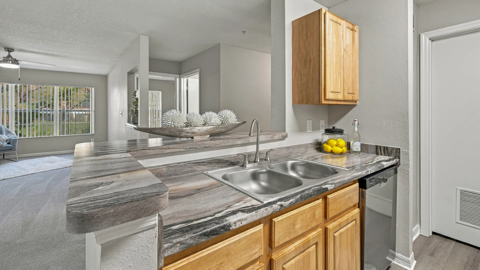 Breakfast bar at Eagle's Pointe featuring a spacious countertop, double-basin sink, wood cabinetry, and an open view into the living room.