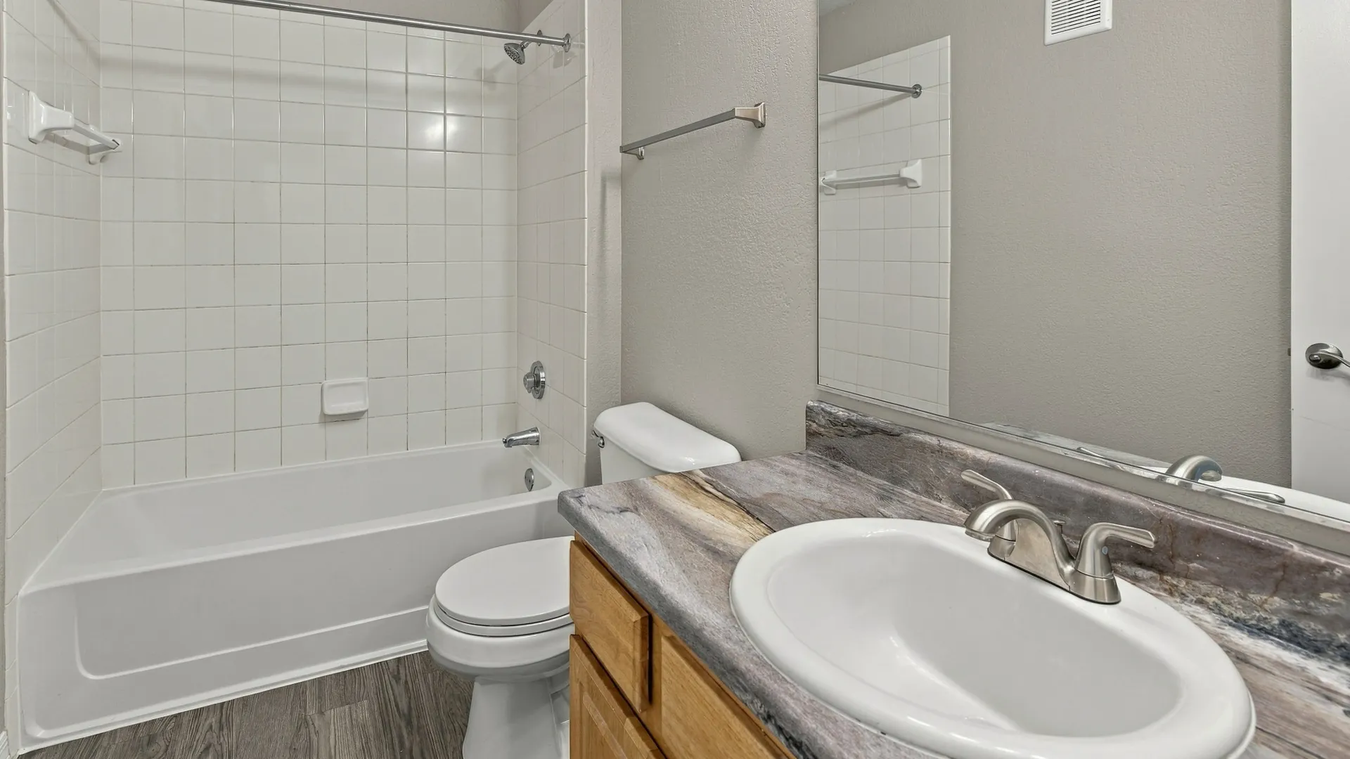 Bathroom in The Port floor plan featuring a spacious vanity with ample counter space, wood cabinetry, a large wall mirror, and a bathtub with a tiled shower surround.
