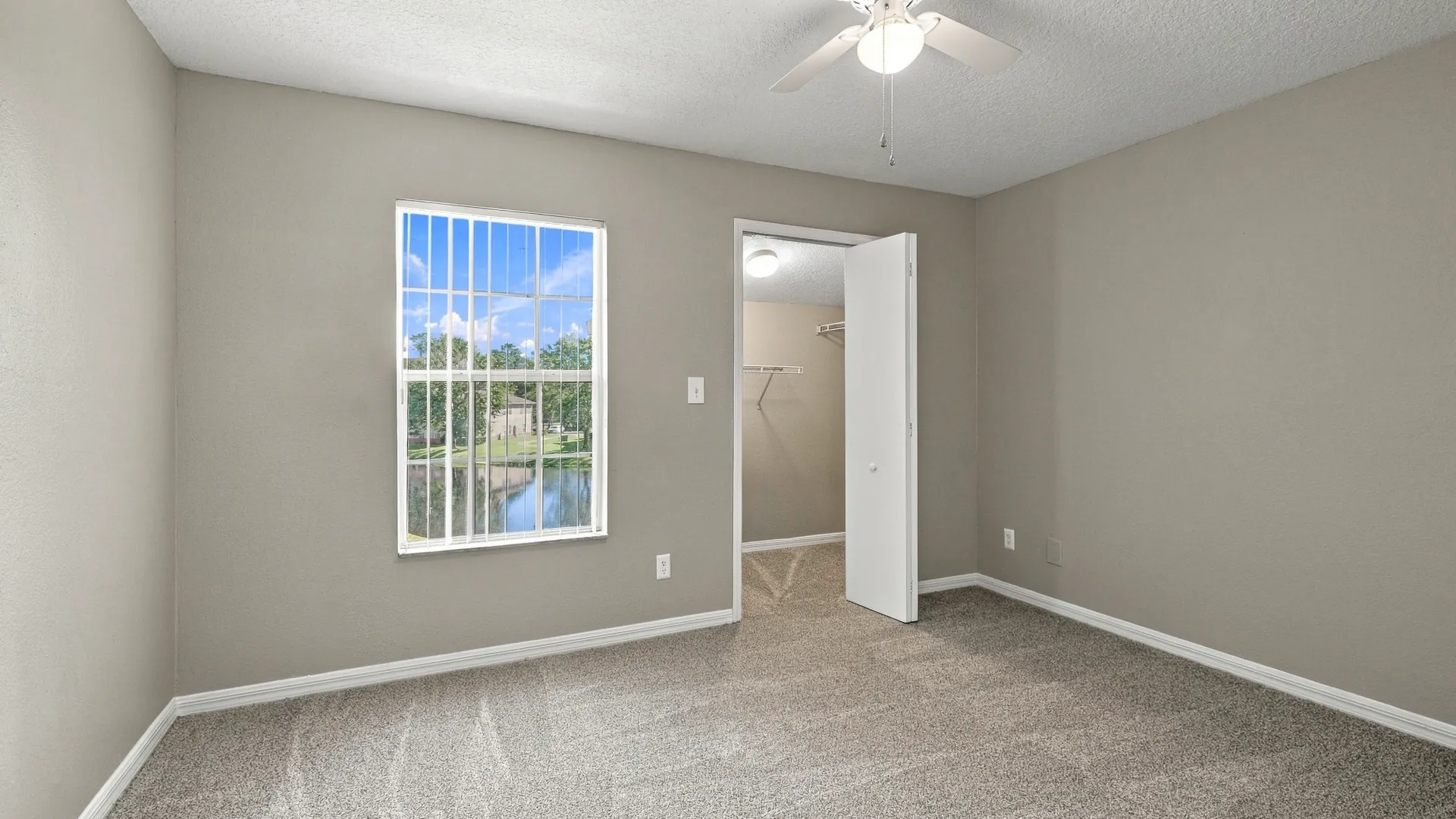 Bedroom in The Port floor plan at Eagle's Pointe featuring plush carpeting, a ceiling fan, a large window with natural light, and a walk-in closet with built-in shelving.