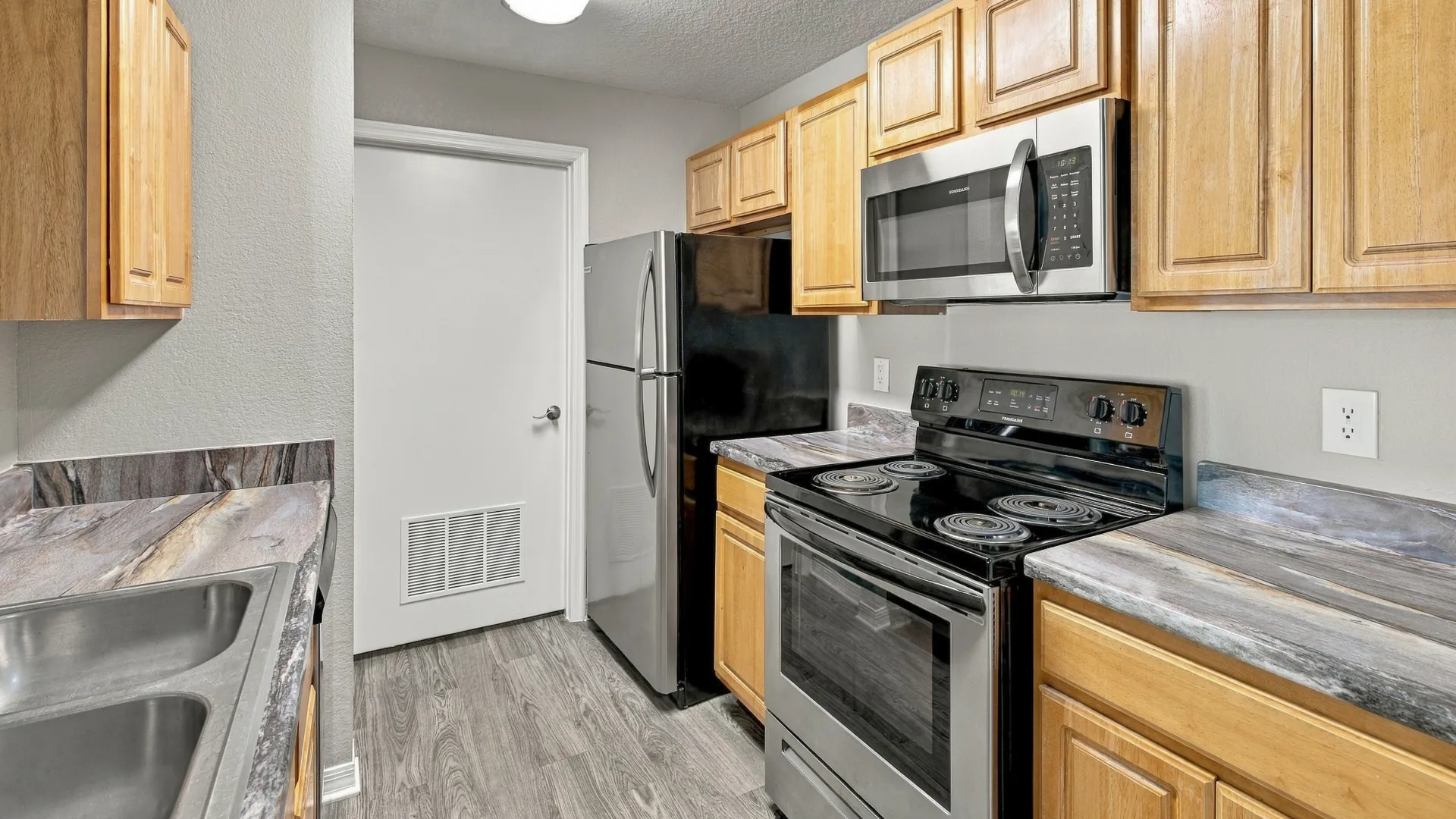 Kitchen in The Port floor plan featuring stainless steel appliances, wood cabinetry, spacious countertops, a double-basin sink, and wood-style flooring.