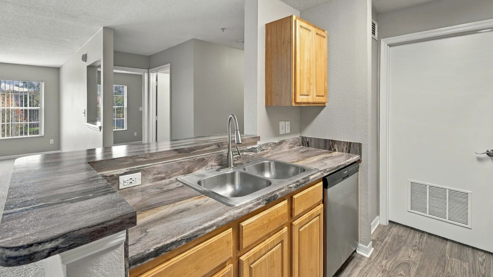 Breakfast bar in The Port floor plan at Eagle's Pointe featuring a raised countertop, double-basin sink, stainless steel dishwasher, and an open connection to the living area.