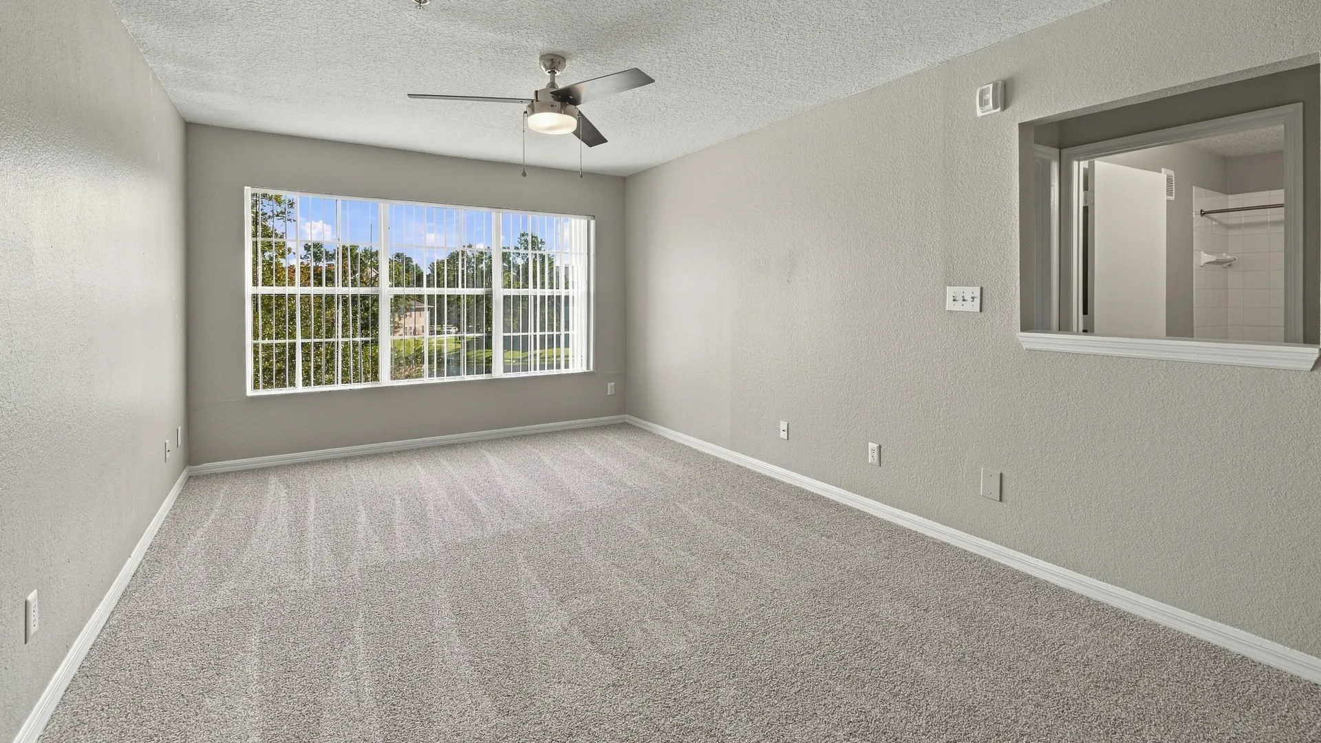 Living room in The Port floor plan at Eagle's Pointe featuring plush carpeting, a ceiling fan, a large window with natural light, and an open-concept layout.