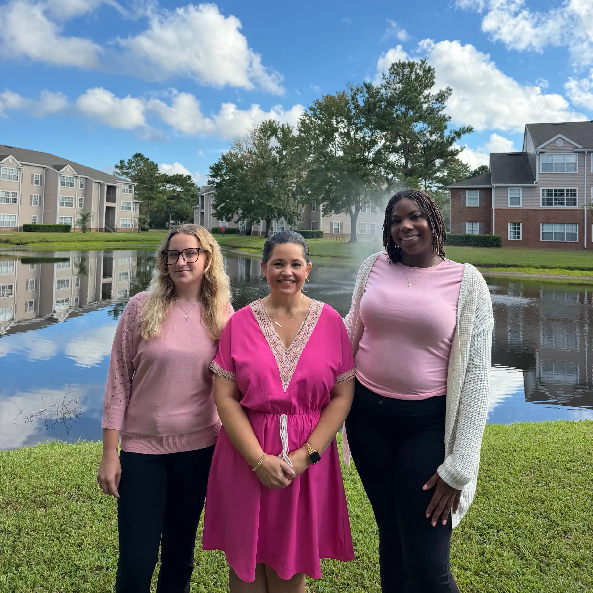 Two Eagles Pointe management and leasing team members standing outdoors by the community pond with apartment buildings in the background.