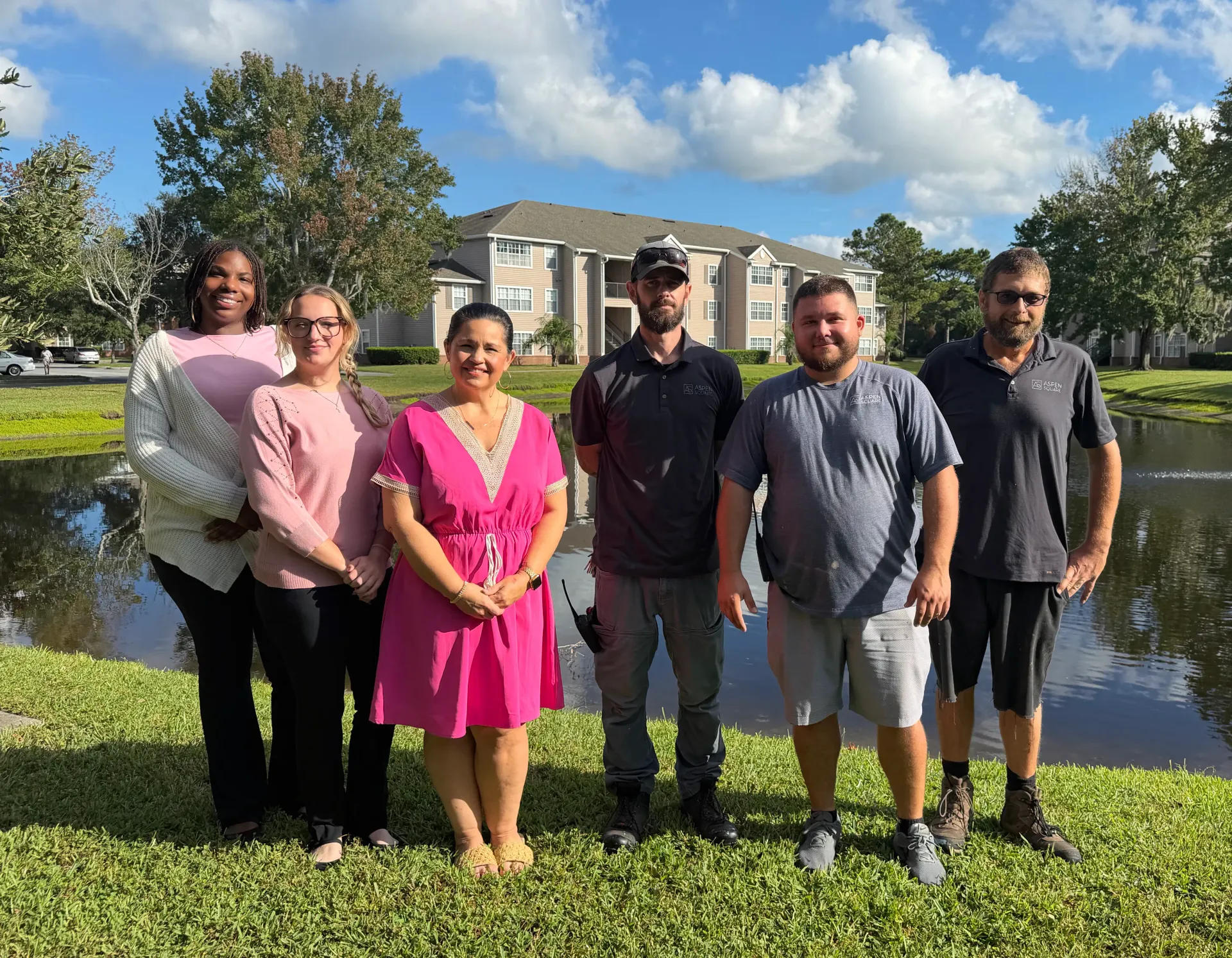 Six Eagle’s Pointe team members standing together outdoors beside the community pond with apartment buildings in the background.