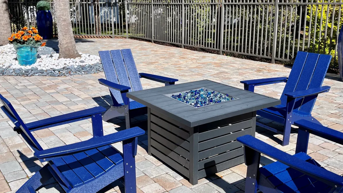 Royal blue Adirondack chairs encircle a glowing fire pit with gleaming shades of blue glass rocks.