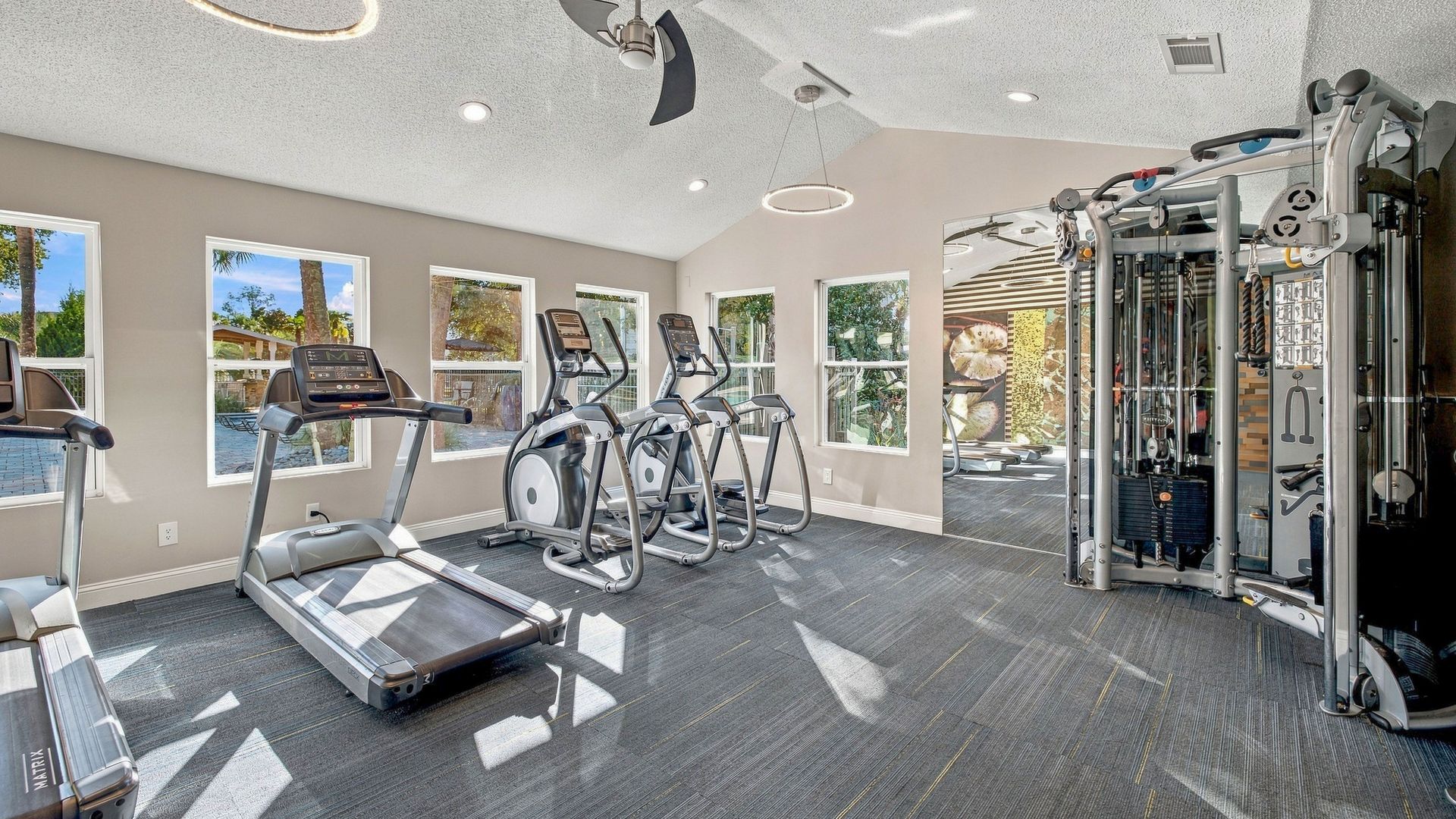 Fitness center at Lanier Landing featuring treadmills, elliptical machines, a multi-station strength-training system, large windows, and an open workout area.