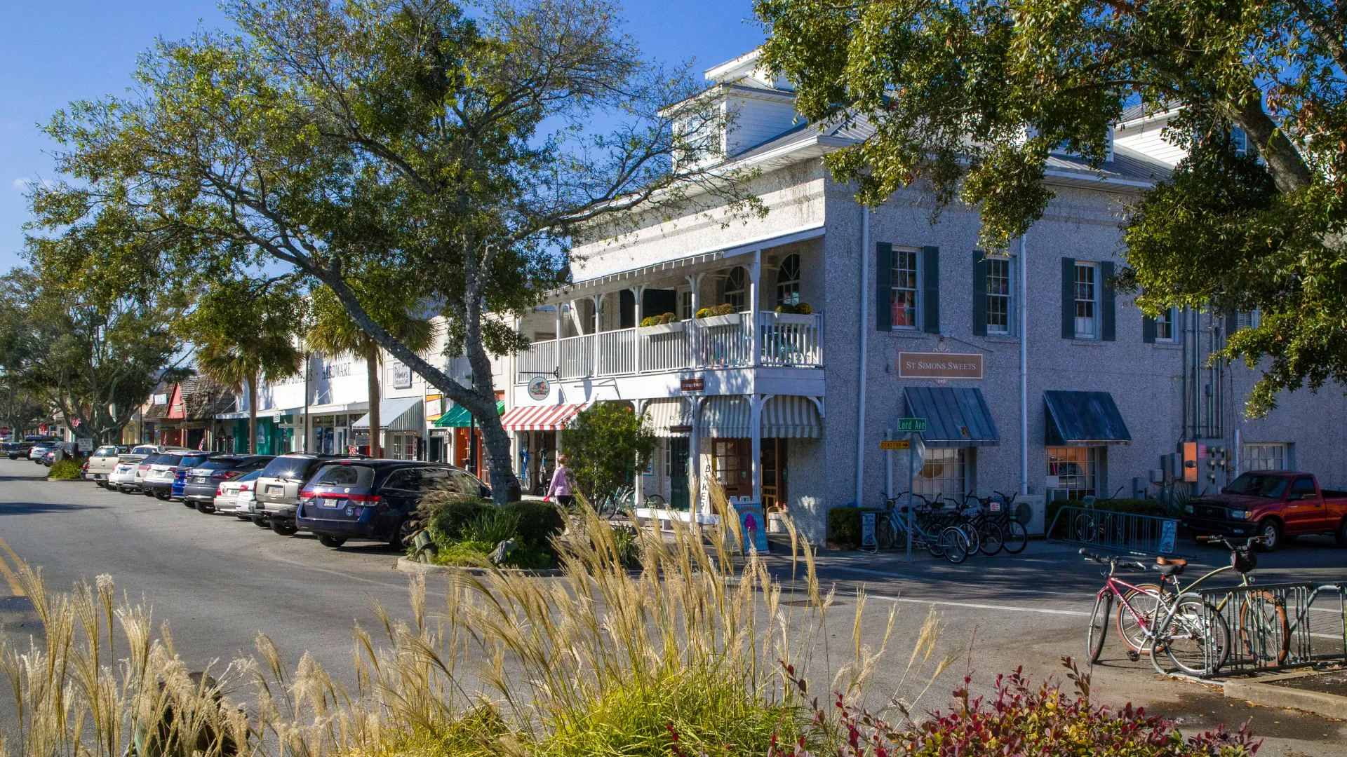 Street view of restaurants and shops on St. Simons Island in Brunswick, GA, with parked cars and bicycles in the foreground.