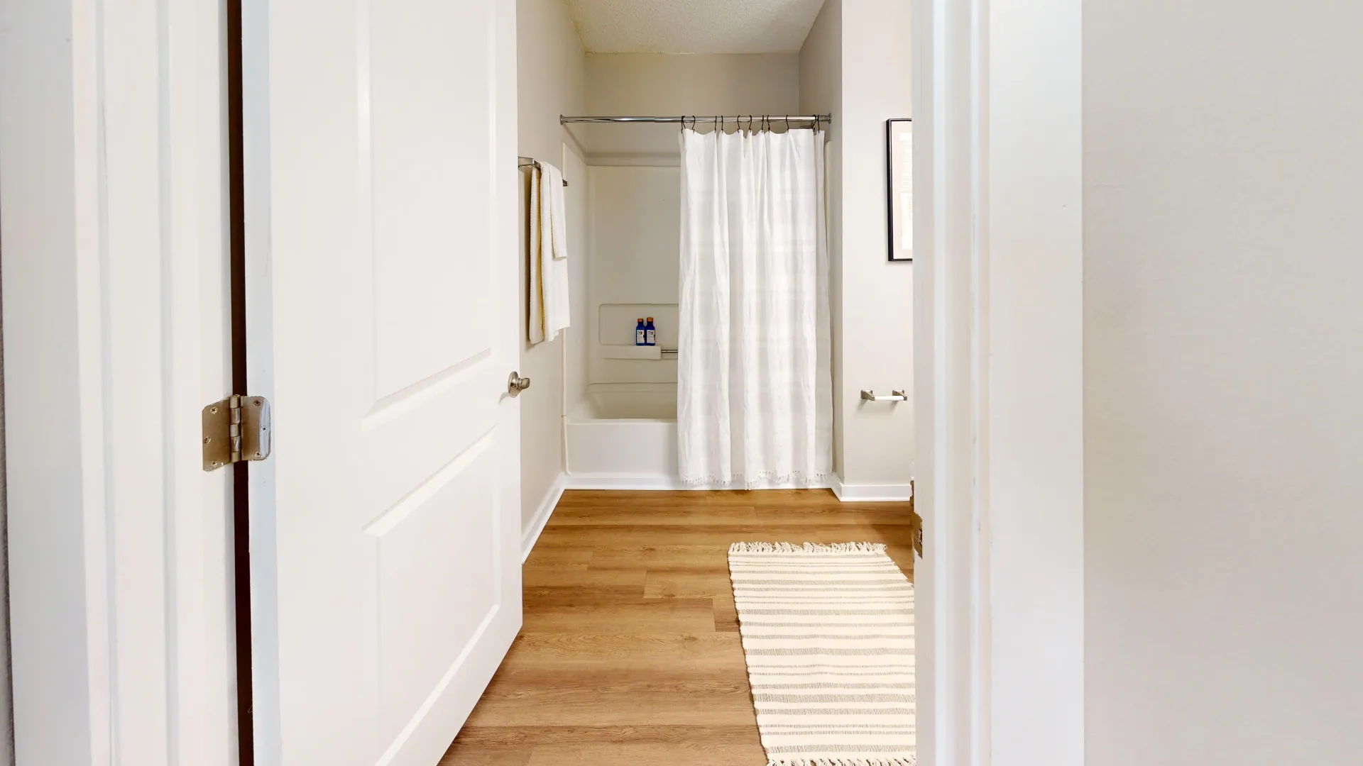 An expansive bathroom featuring a luxurious shower/tub combo, elegant wood-style flooring, and additional square footage for added comfort.