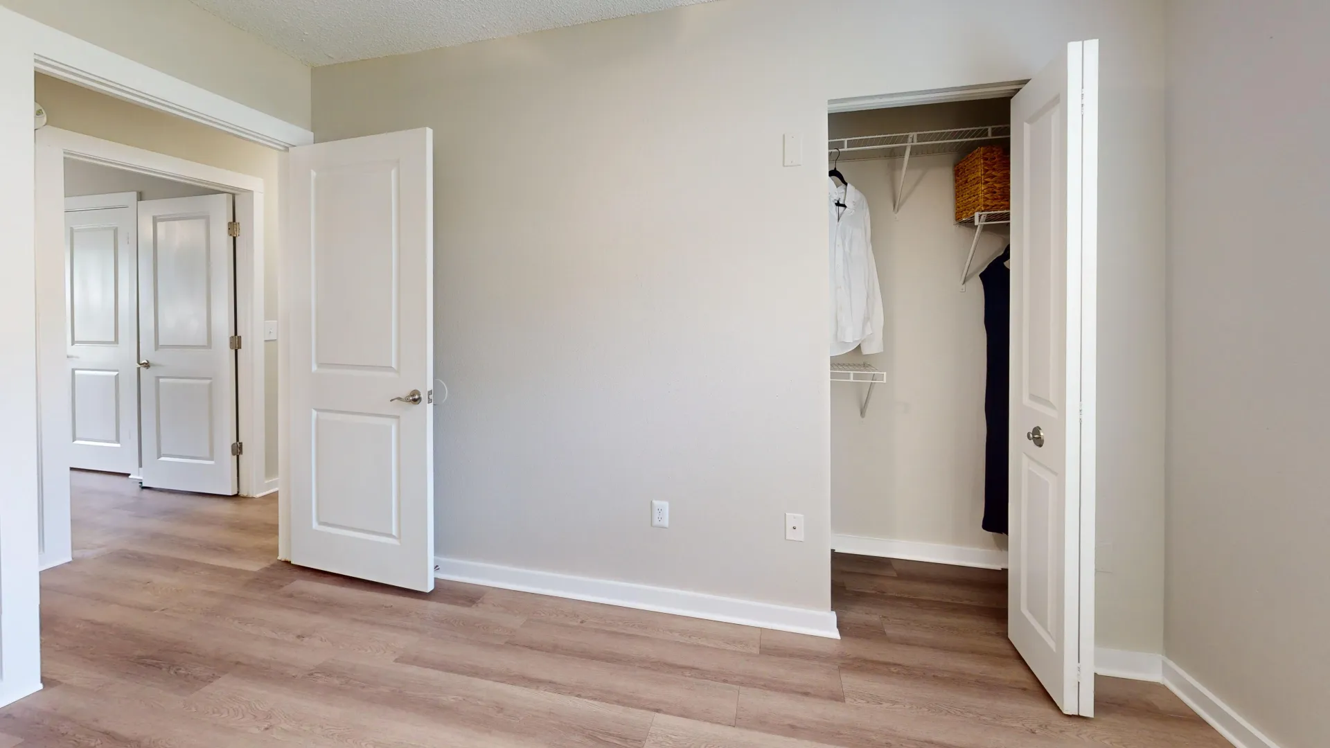Inside a secondary bedroom, unveil a variety of open-wire shelving racks behind a bi-fold closet door, offering stylish wardrobe organization.