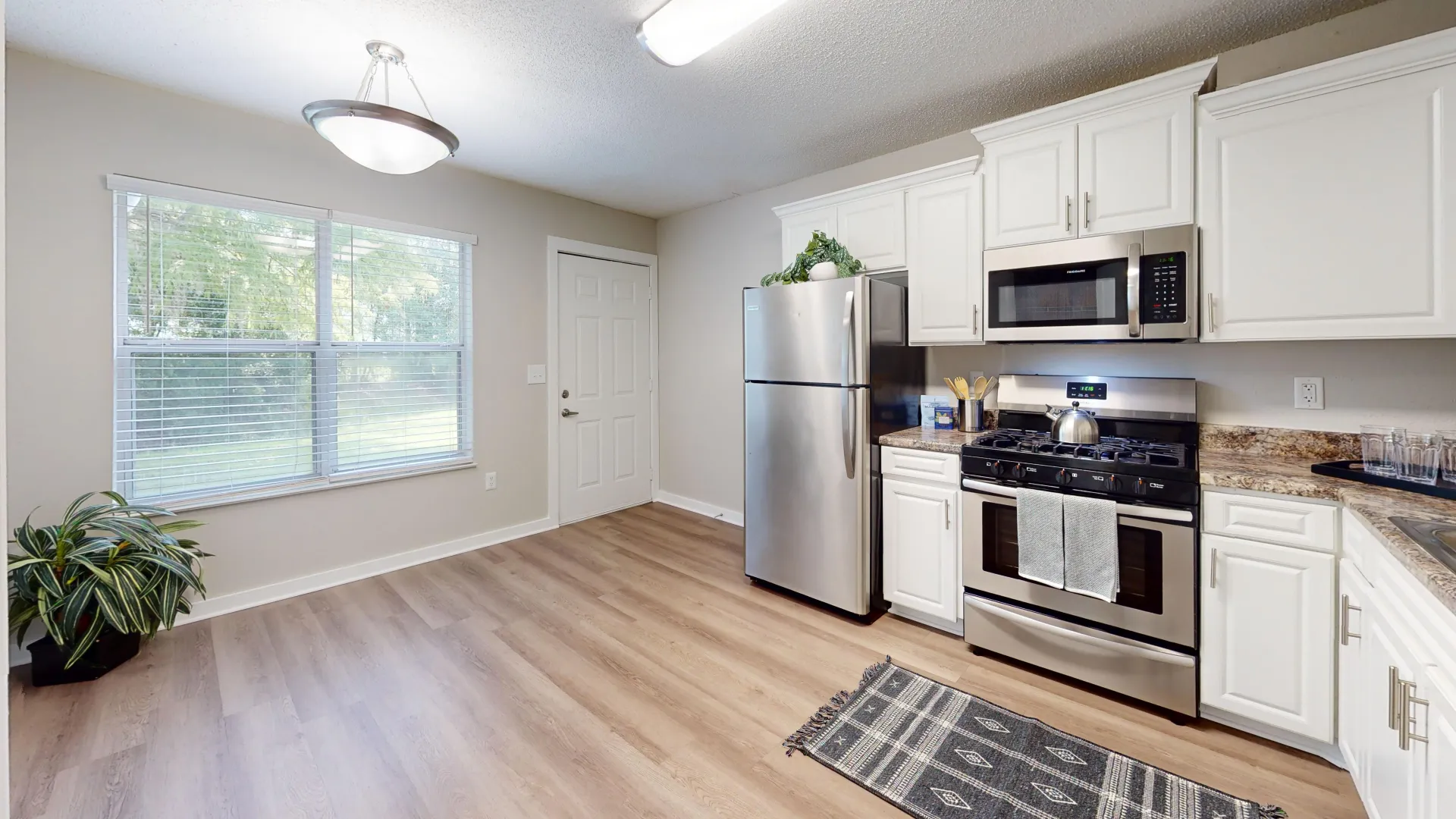 An extra spacious kitchen adorned with a huge double-wide window, gleaming stainless-steel appliances, and additional space for a table with a dedicated lighting fixture.