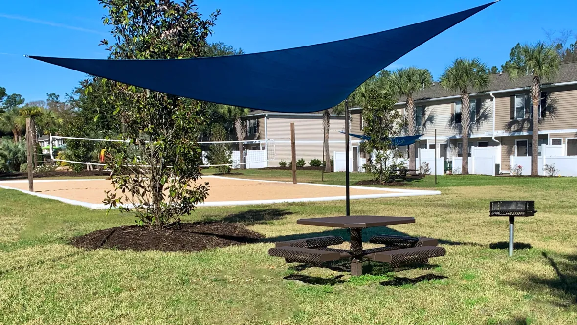 A prime picnic zone with a spacious picnic table and sail shade, nestled beside the sandy volleyball court.