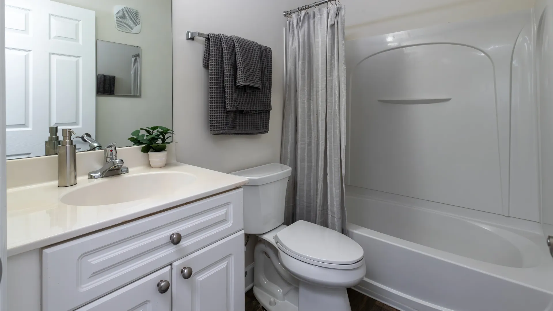 Modern bathroom with white vanity, sink, toilet, and bathtub at The Foundry Apartments, featuring clean design and stylish decor.