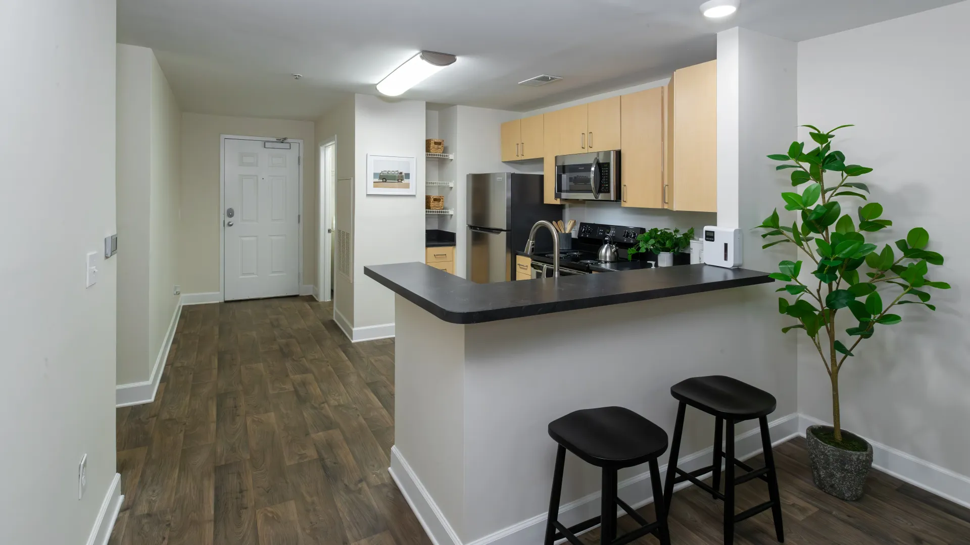 Modern kitchen featuring stainless steel appliances, bar seating, and wood-style flooring.