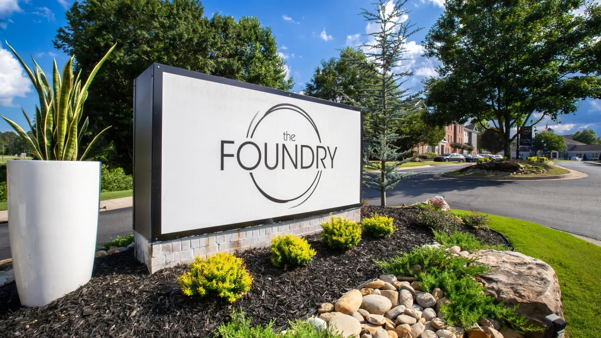 The front signage of the community with The Foundry logo on a white backdrop and a tall white planter and elegant landscape