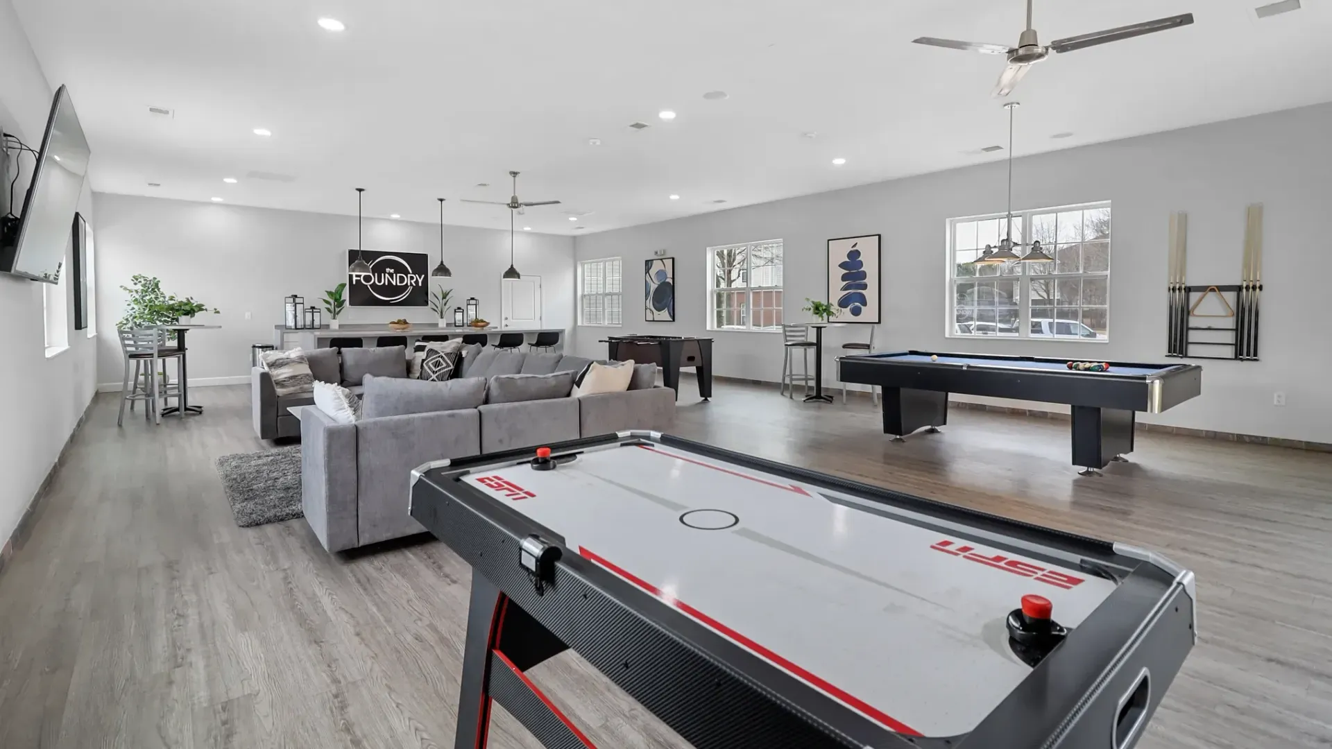 An air hockey table and billiard table poised for play along with a massive sectional couch