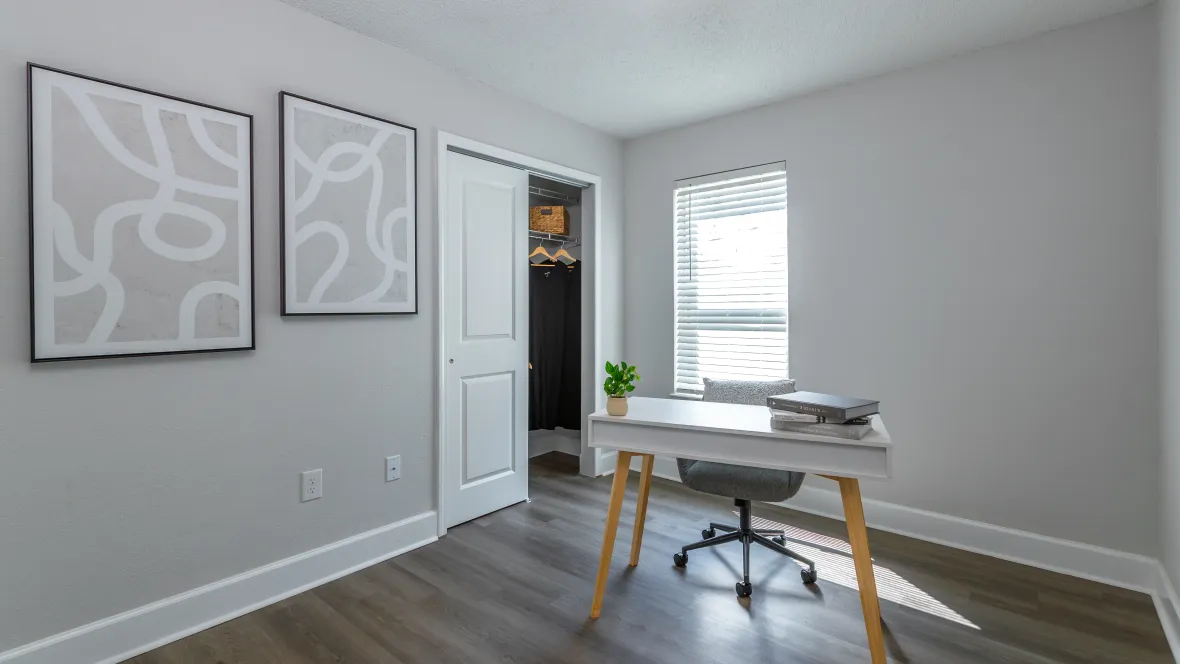 A brightly lit bedroom space converted into an office area with brilliant overhead lighting and a spacious closet, offering flexibility for various room purposes.