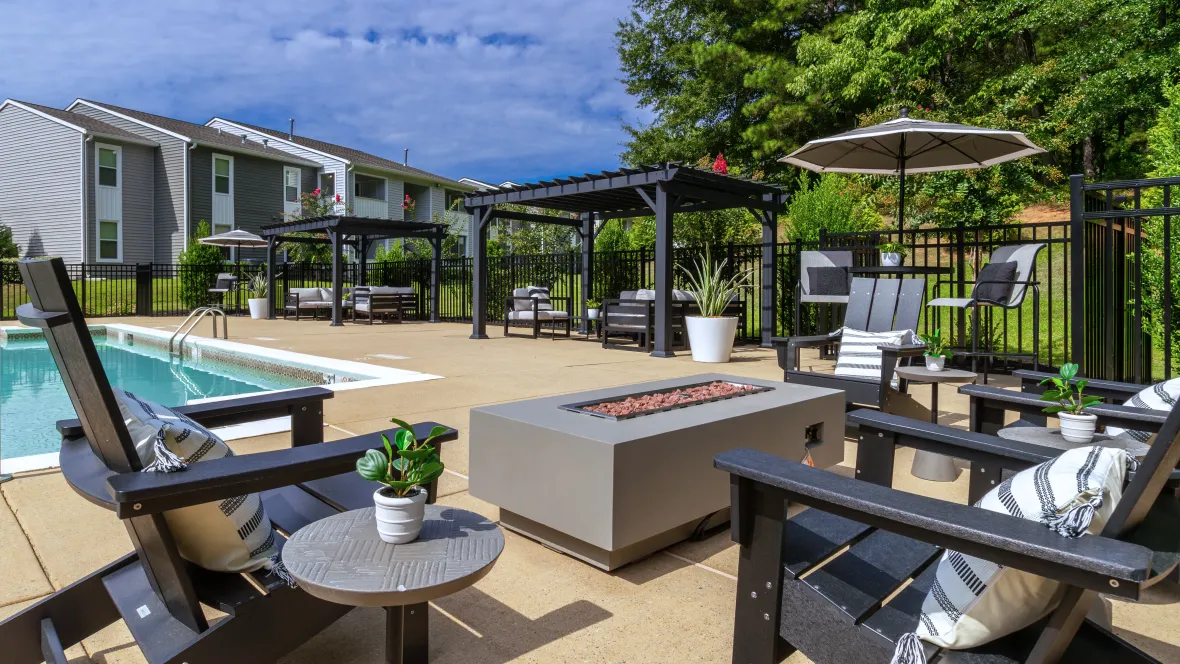 A convenient fireside setting with a large fire pit and black Adirondack chairs at the pool deck's end, complemented by poolside pergolas, offering warmth and cozy relaxation zones.